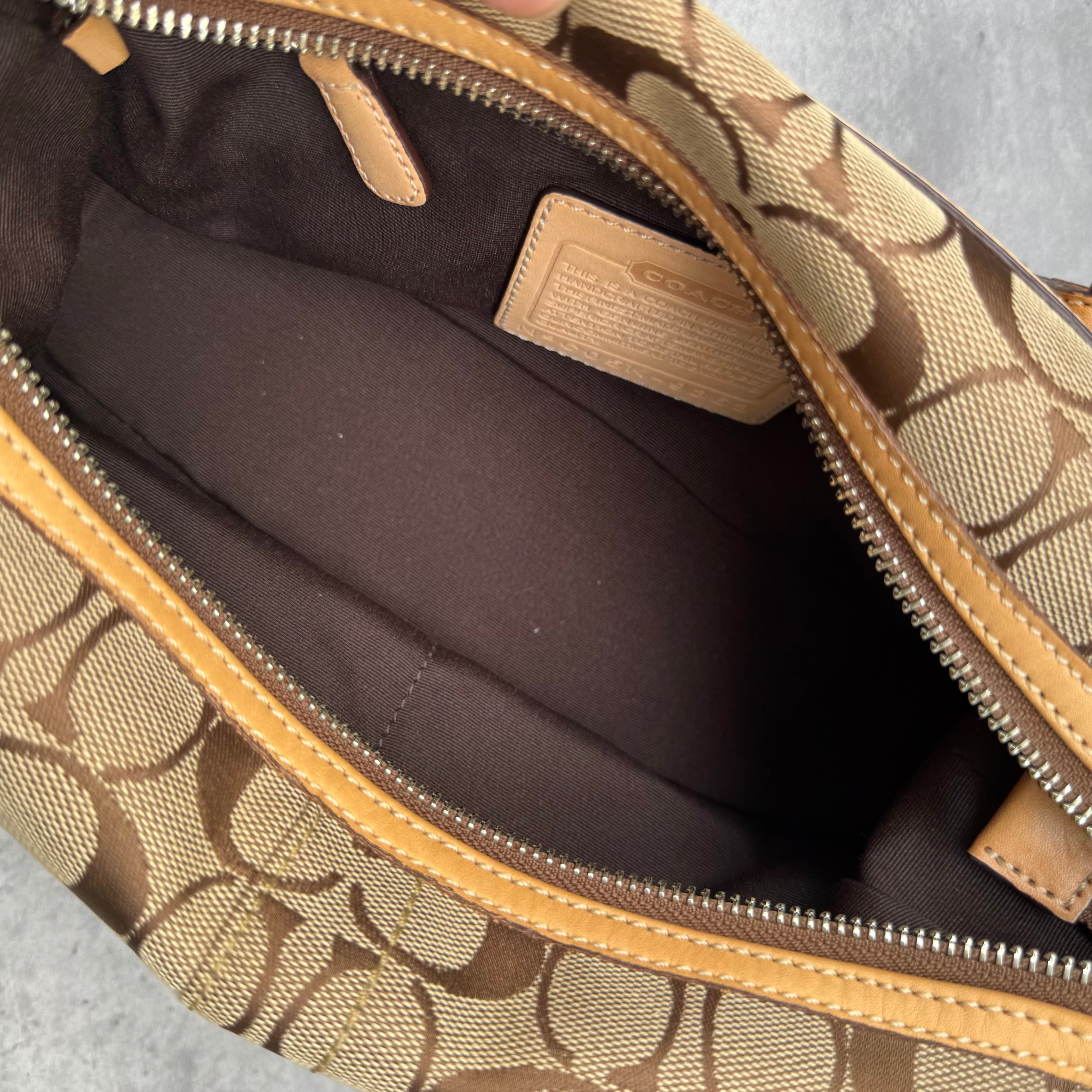 Coach Signature Coated Canvas Tassel Shoulder Bag in brown monogram print with tan leather trim and tassel detail.