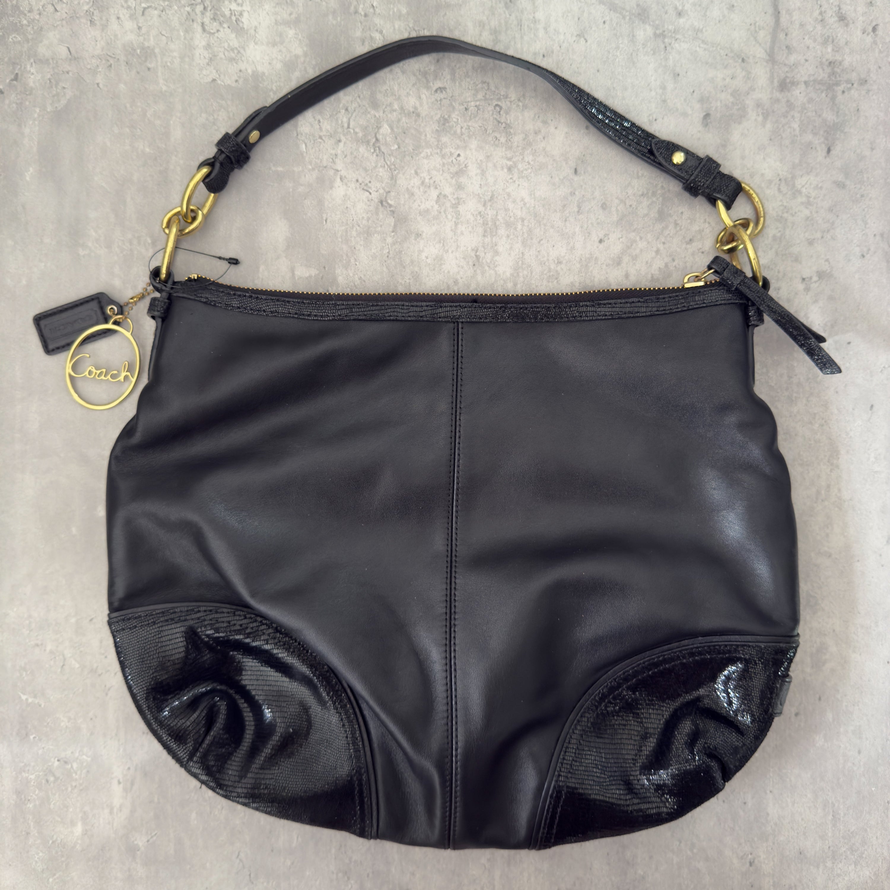 Coach Signature Cursive Logo Shoulder Bag in black leather with gold-tone hardware, featuring a spacious fabric-lined interior and signature Coach charm.