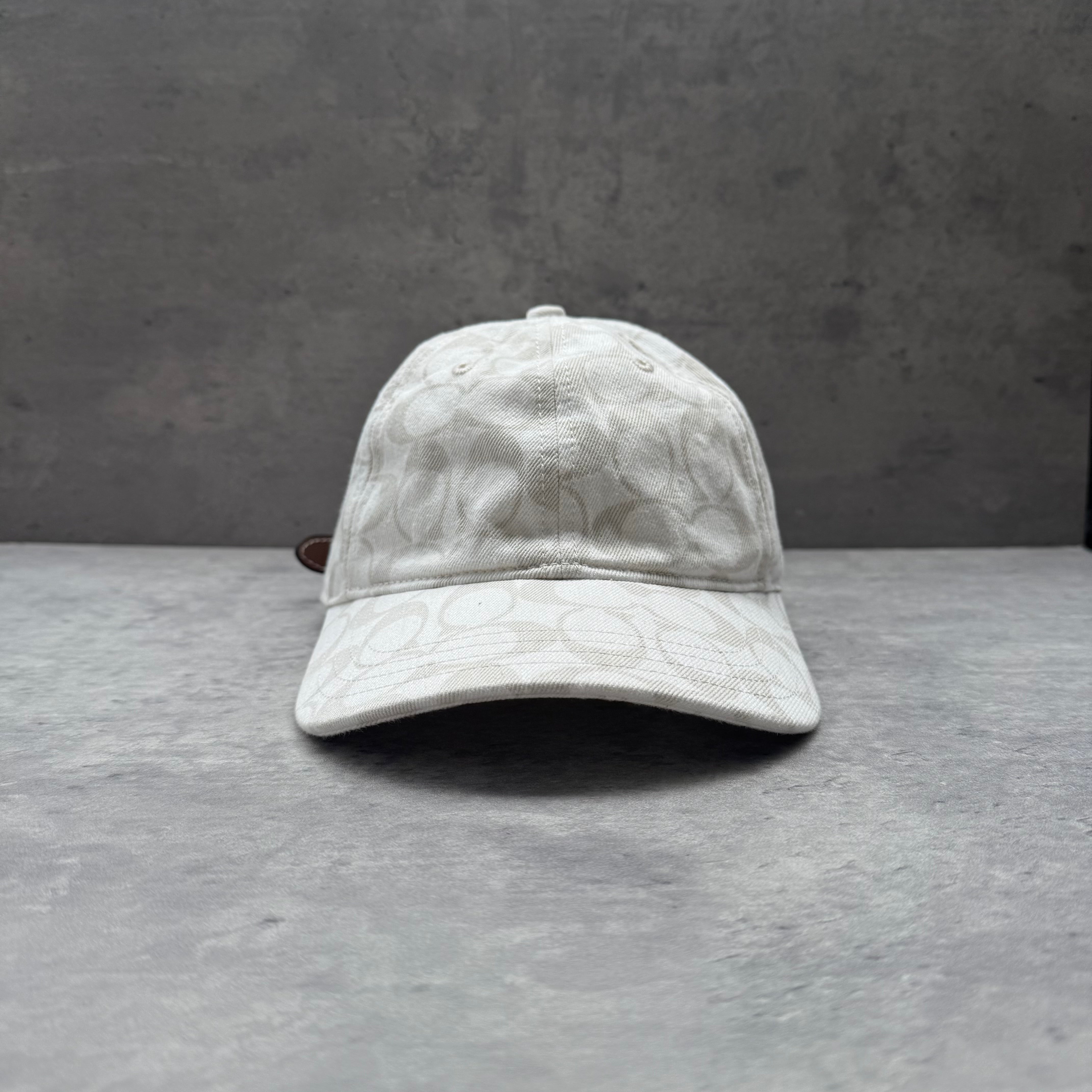 Coach Signature Denim Baseball Cap in white with monogram pattern and adjustable brown leather strap.