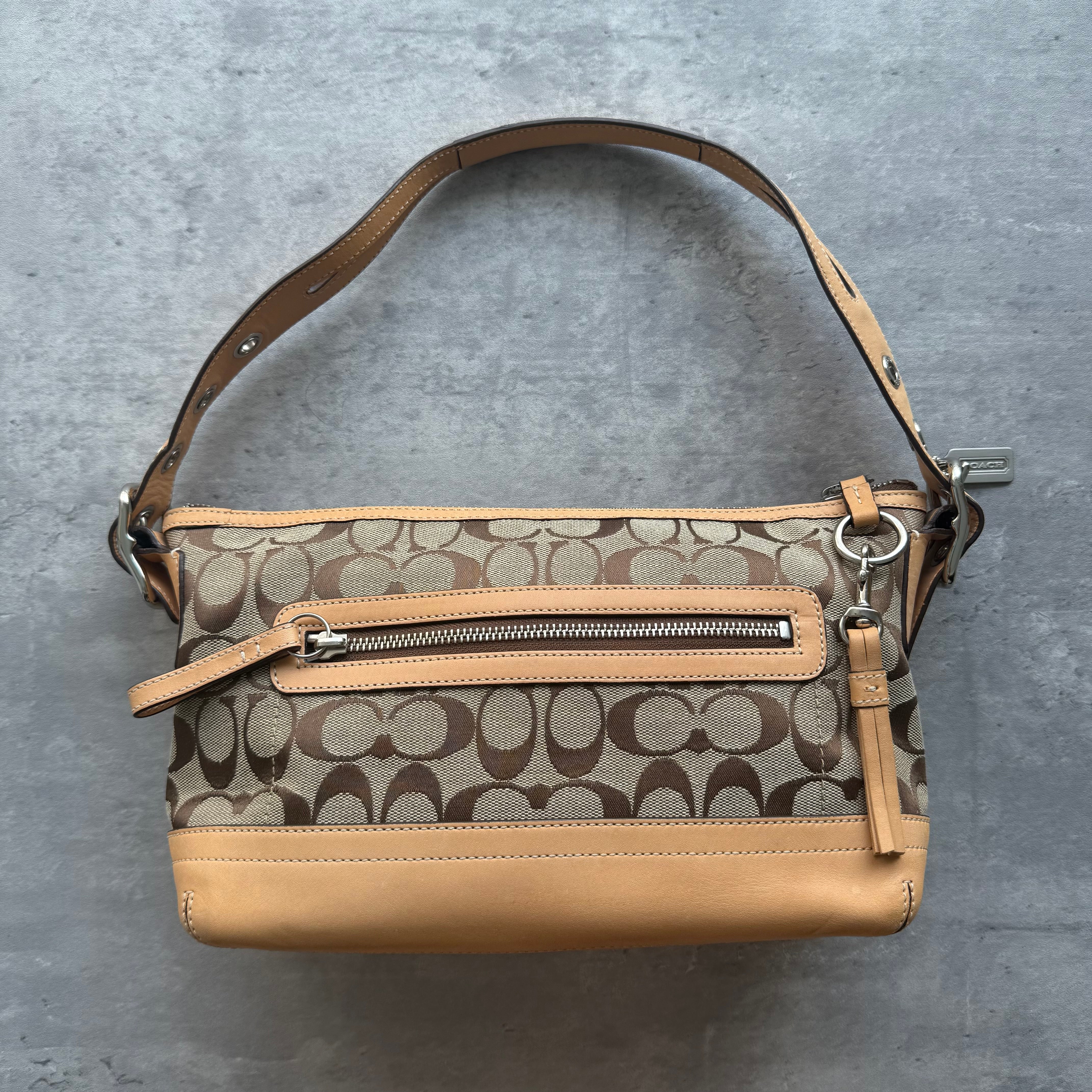 Coach Signature East West Shoulder Bag in beige monogram canvas with tan leather trim, silver hardware, and grommet-detailed strap.