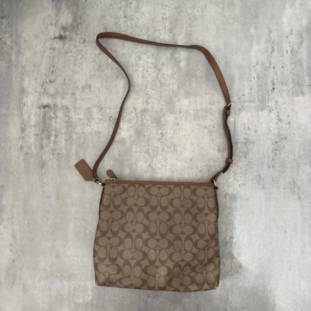 Coach Signature File Crossbody Bag in beige and brown monogram canvas, featuring leather trim, gold-tone hardware, and an adjustable crossbody strap.