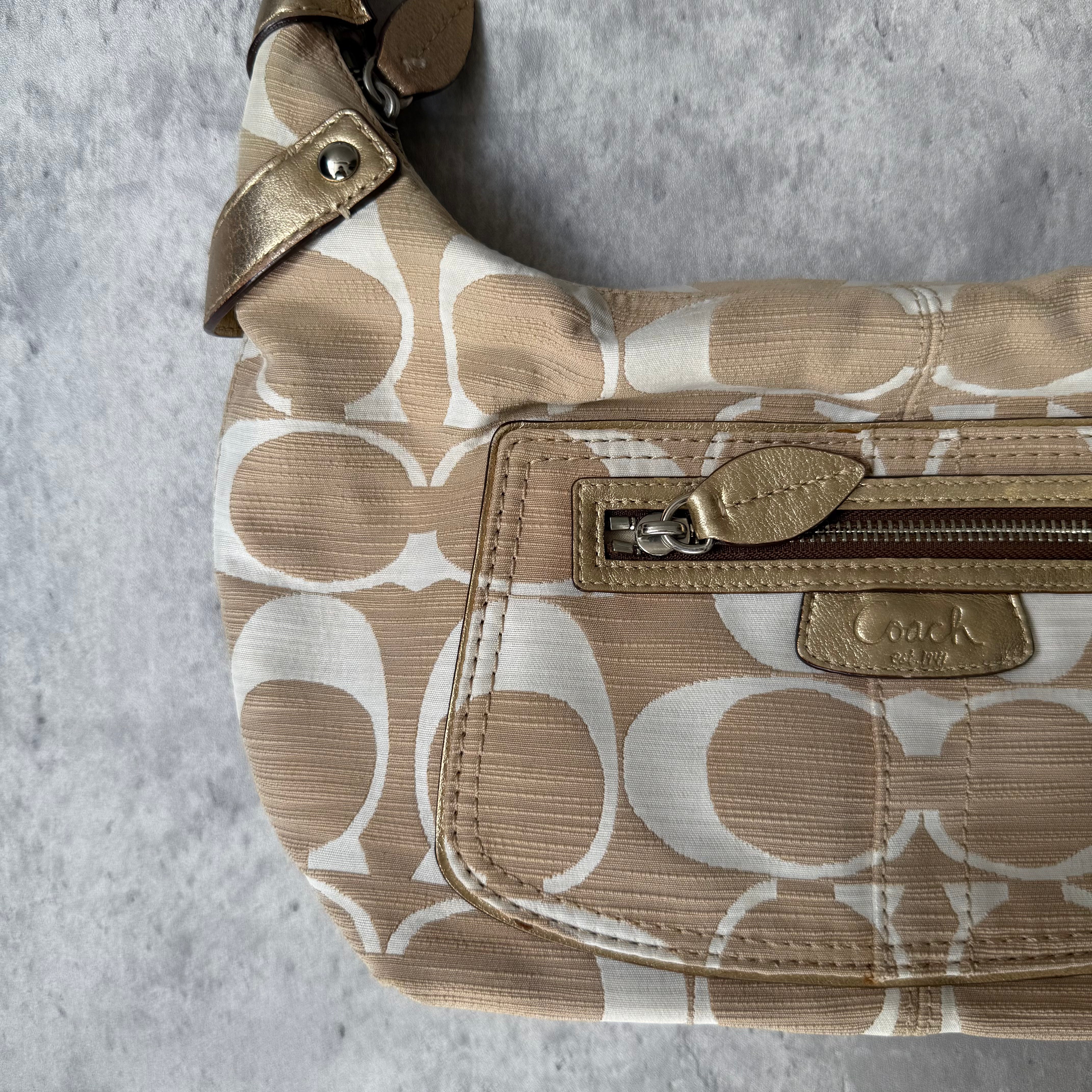 Coach Signature Penelope Hobo Shoulder Bag in beige and white canvas with metallic trim, front zip pocket, and silver-tone hardware.