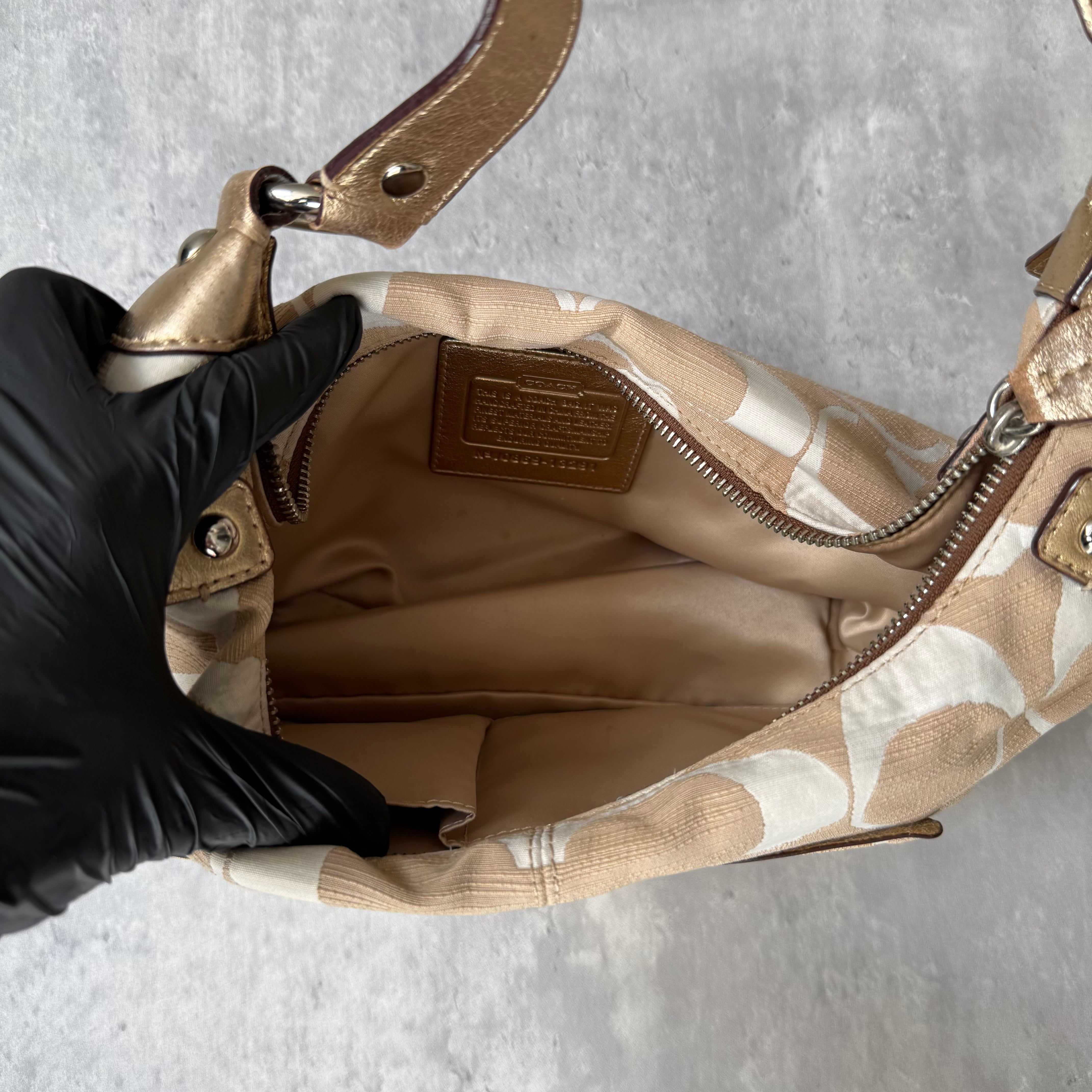 Coach Signature Penelope Hobo Shoulder Bag in beige and white canvas with metallic trim, front zip pocket, and silver-tone hardware.