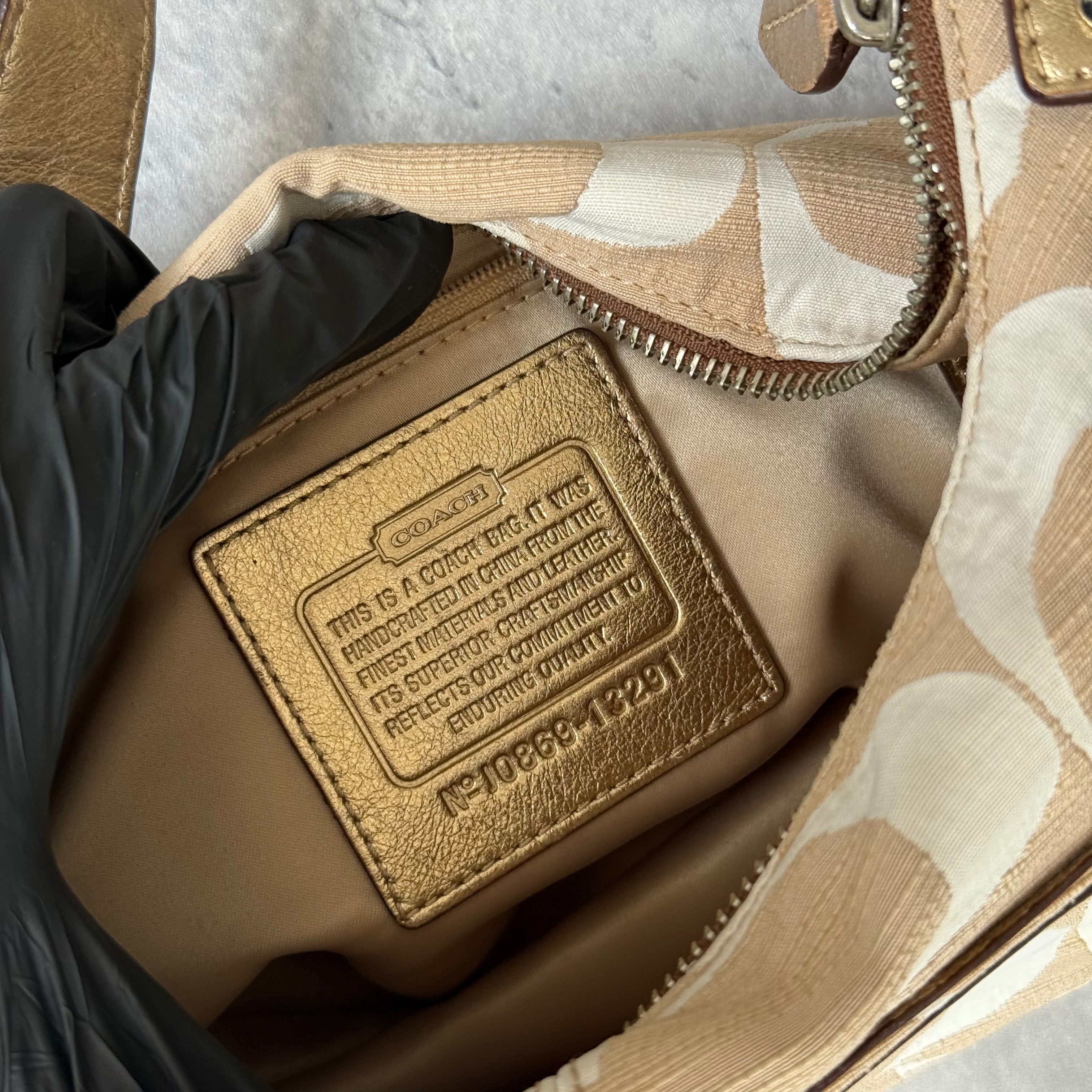 Coach Signature Penelope Hobo Shoulder Bag in beige and white canvas with metallic trim, front zip pocket, and silver-tone hardware.