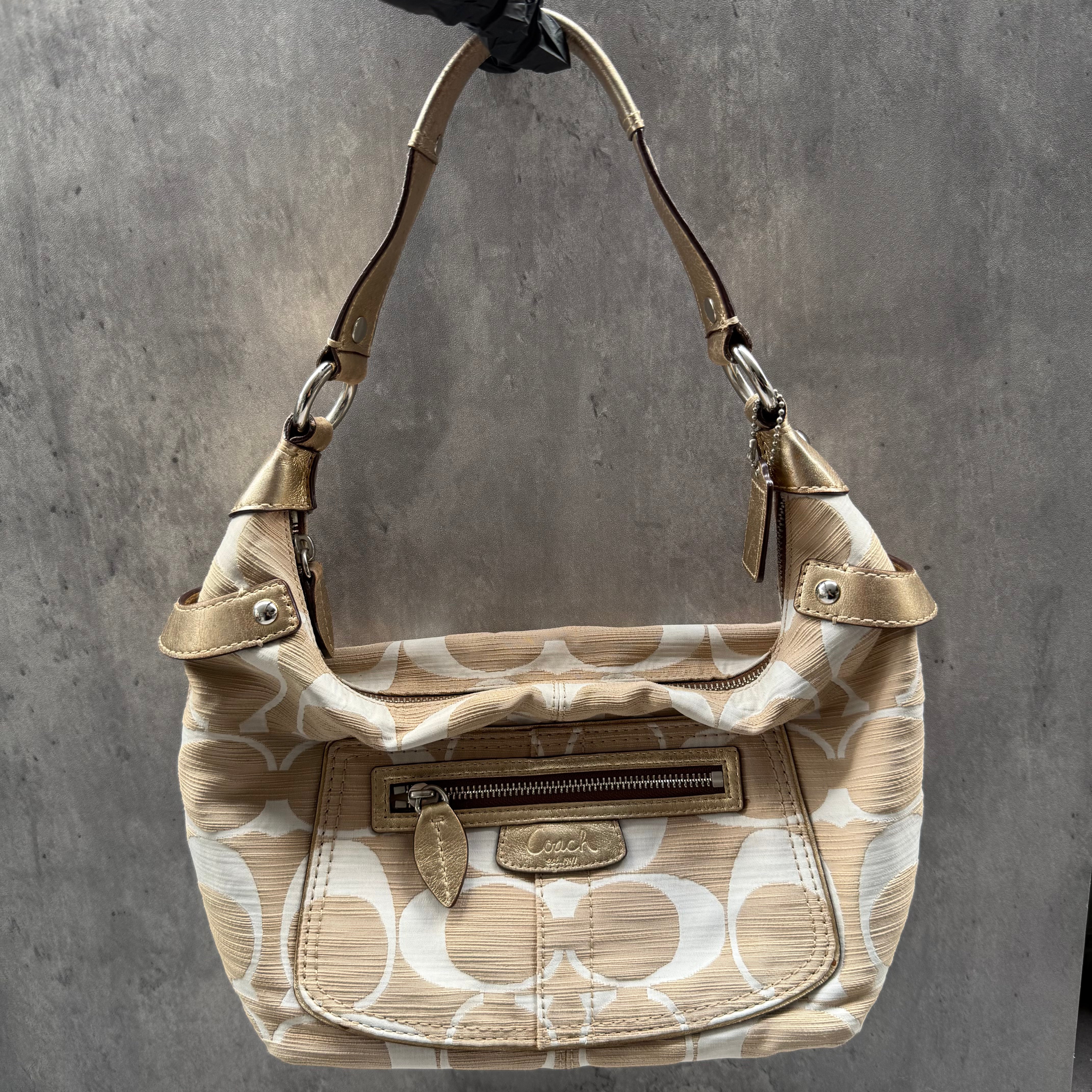 Coach Signature Penelope Hobo Shoulder Bag in beige and white canvas with metallic trim, front zip pocket, and silver-tone hardware.