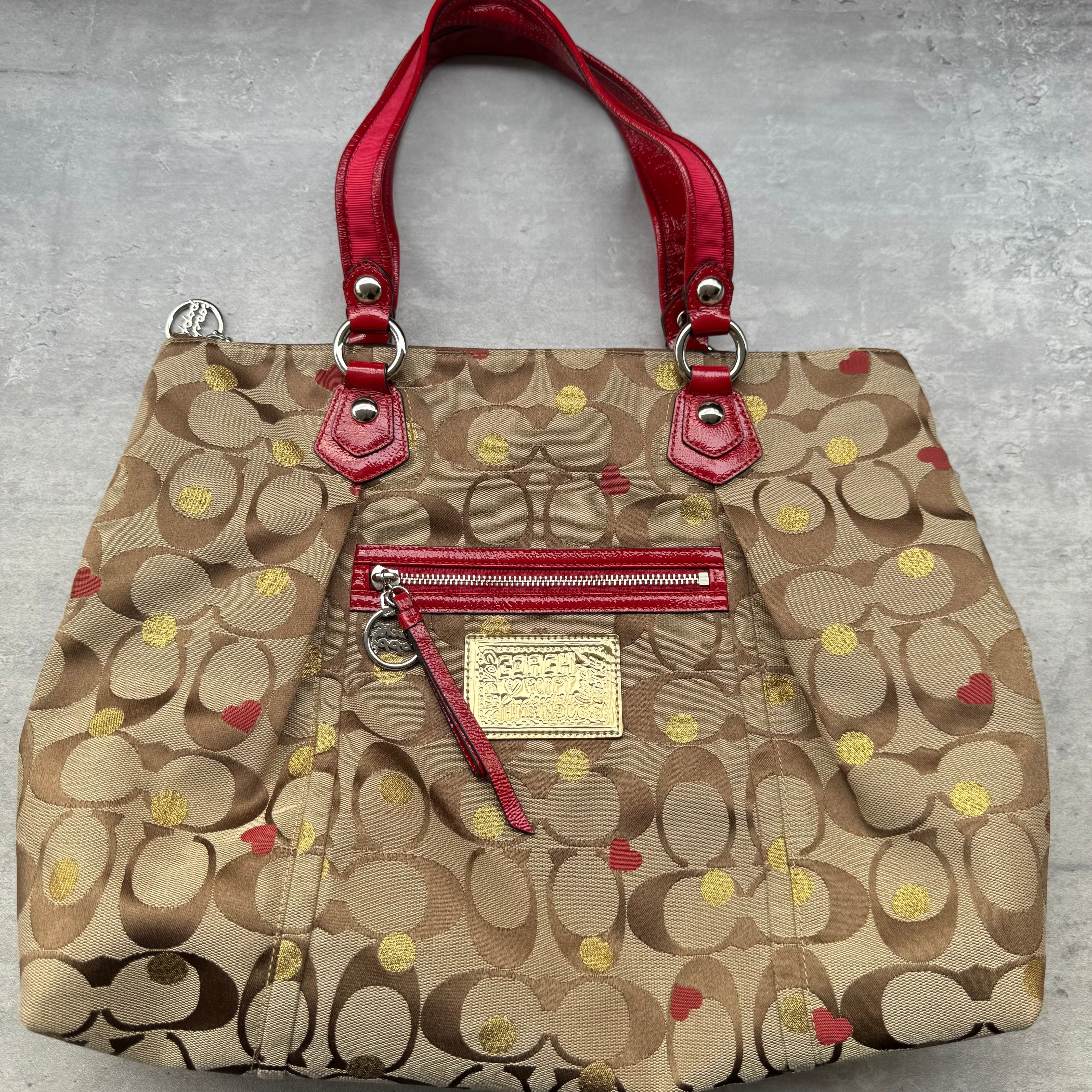 Coach Signature Poppy Laura Secret Admirer Tote Bag in brown monogram canvas with red and gold heart dot accents and red patent leather trim.