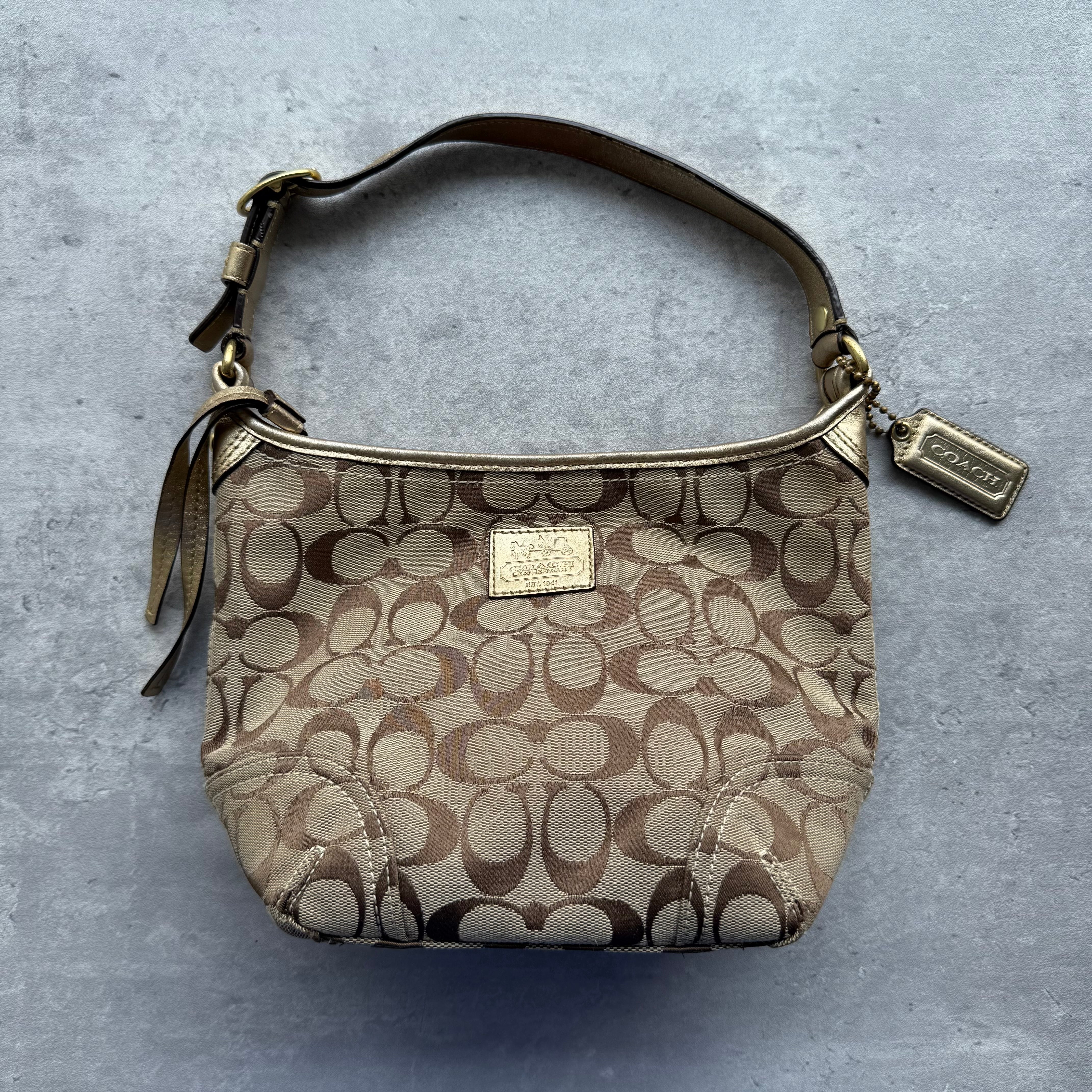 Coach Signature Sacoche Shoulder Bag in beige jacquard with gold leather trim, adjustable strap, and light purple fabric lining.
