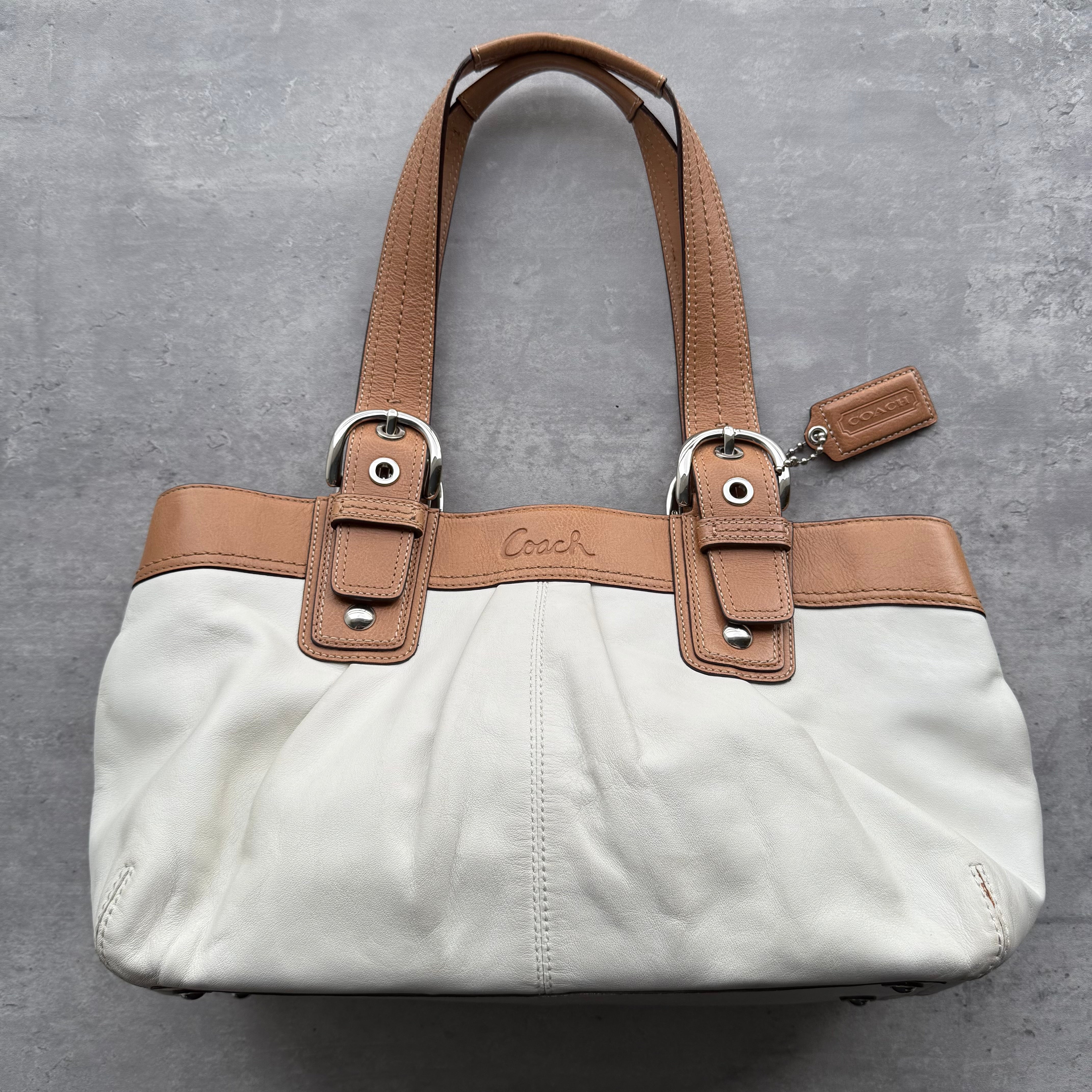 Coach Soho Buckle Tote Bag in white canvas with tan leather trim, buckle accents, and dual shoulder straps.
