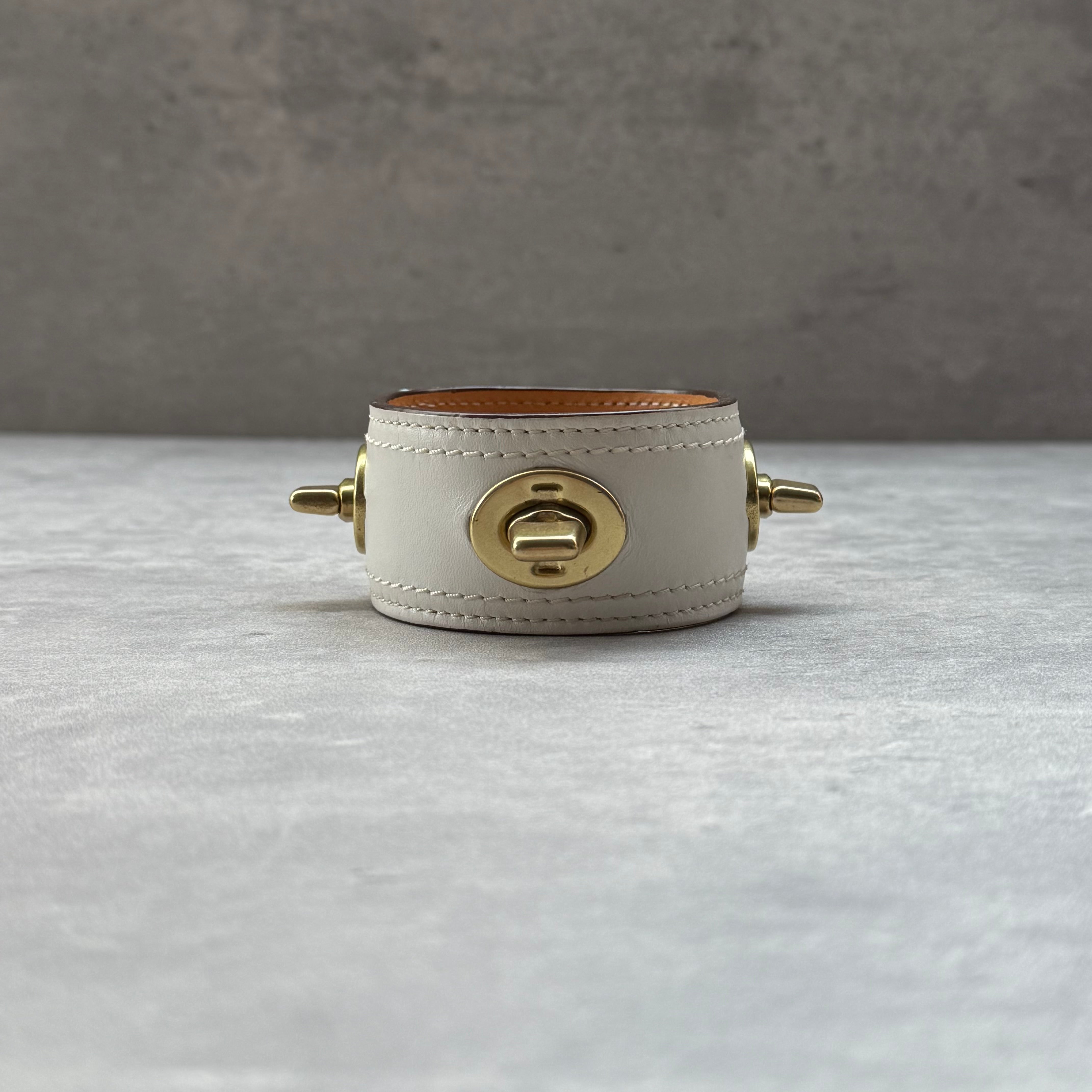 Coach Turnlock Cuff Bracelet White, crafted in white leather with gold-tone turnlock hardware and tan leather lining.