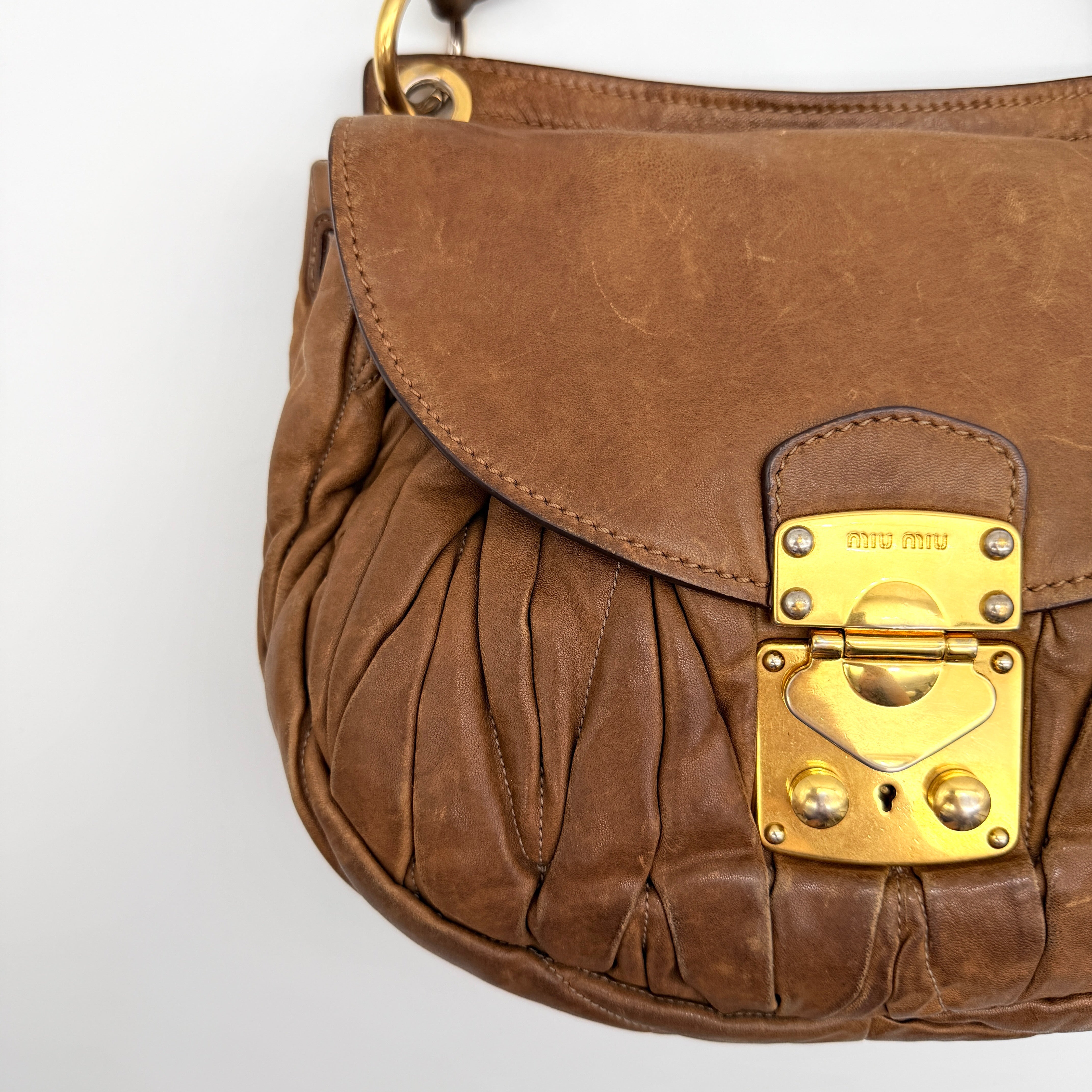 Miu Miu brown Matelasse Coffer Hobo bag with gold hardware, detachable strap, and dust bag displayed on a flat surface.