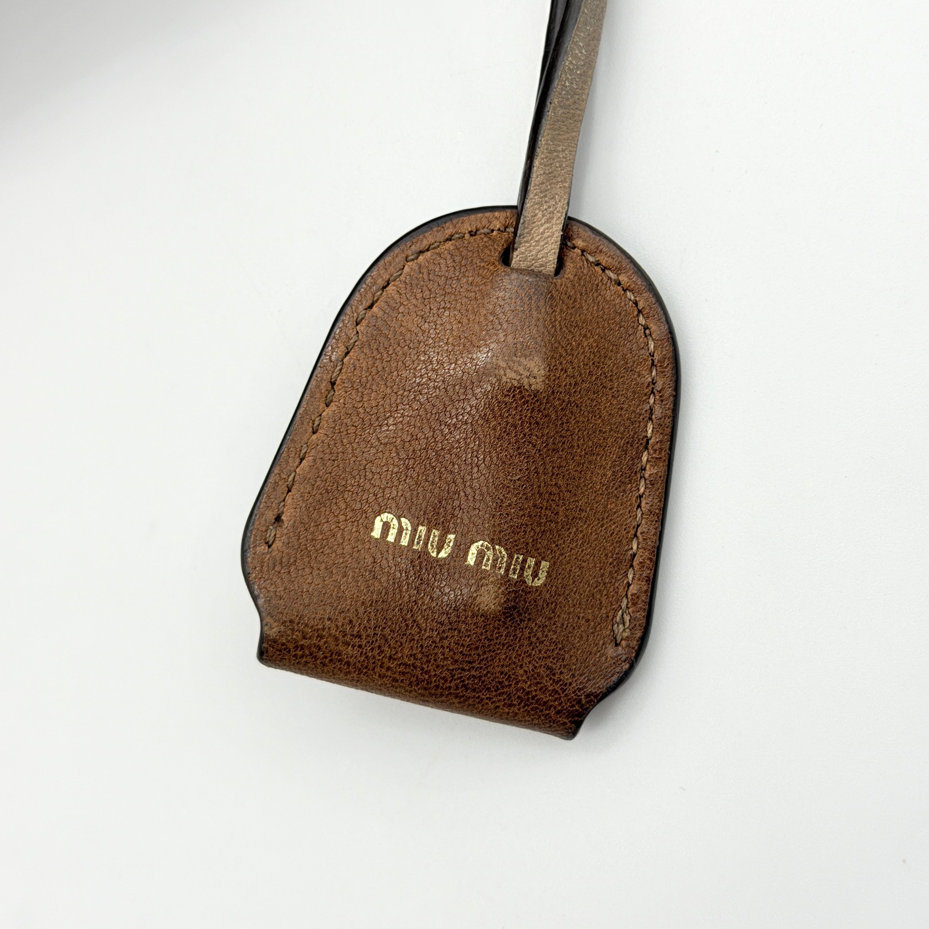 Miu Miu brown Matelasse Coffer Hobo bag with gold hardware, detachable strap, and dust bag displayed on a flat surface.