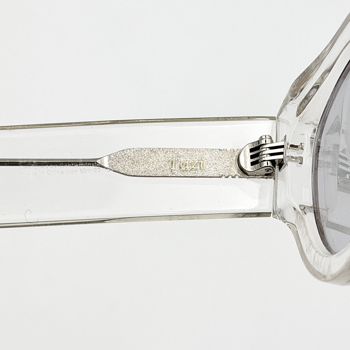 Gentle Monster Tazi transparent sunglasses with grey lenses and clear acetate frame, softly styled alongside the branded case.