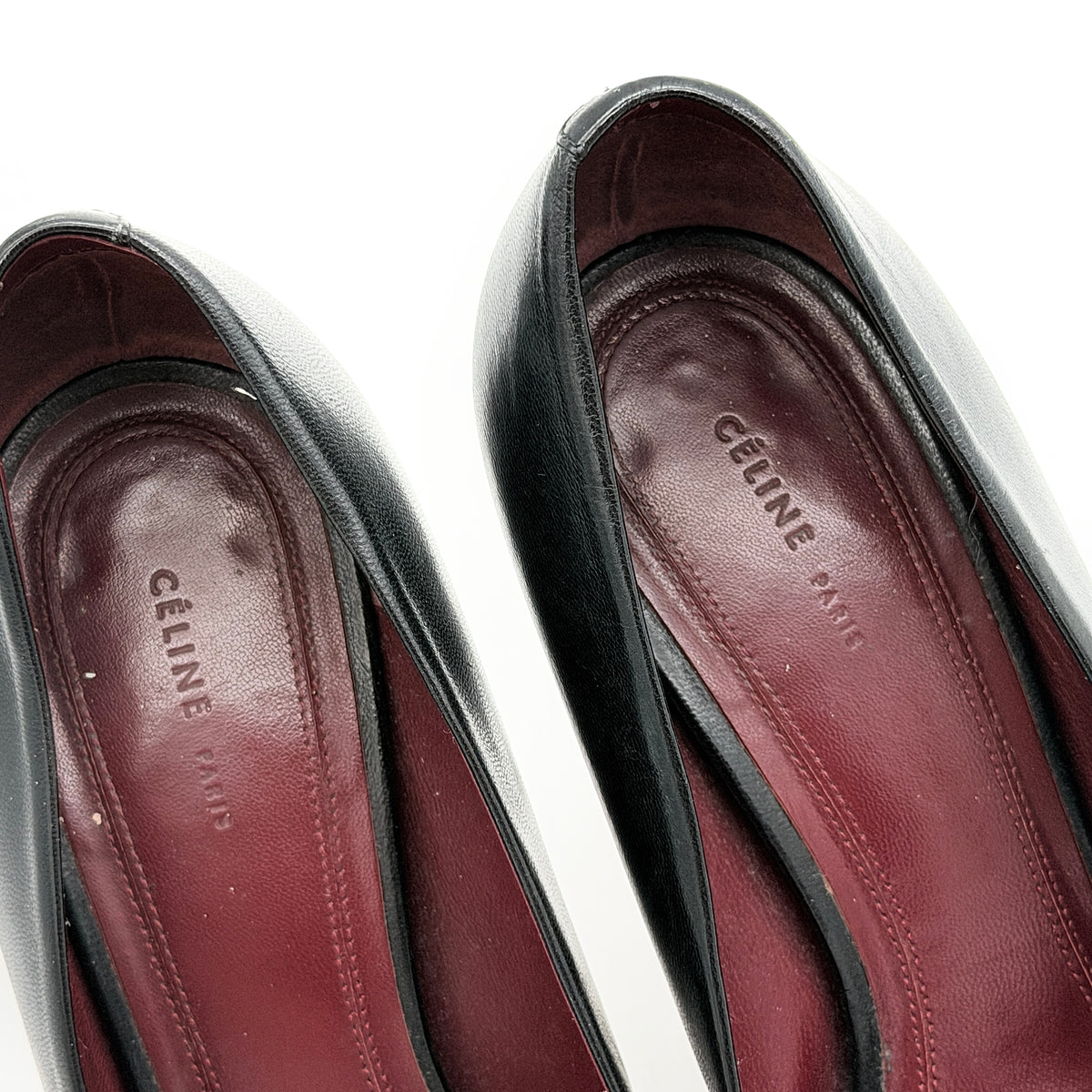 A pair of black leather Celine stiletto heels with pointed toes and burgundy insoles, shown in a softly lit studio setting.