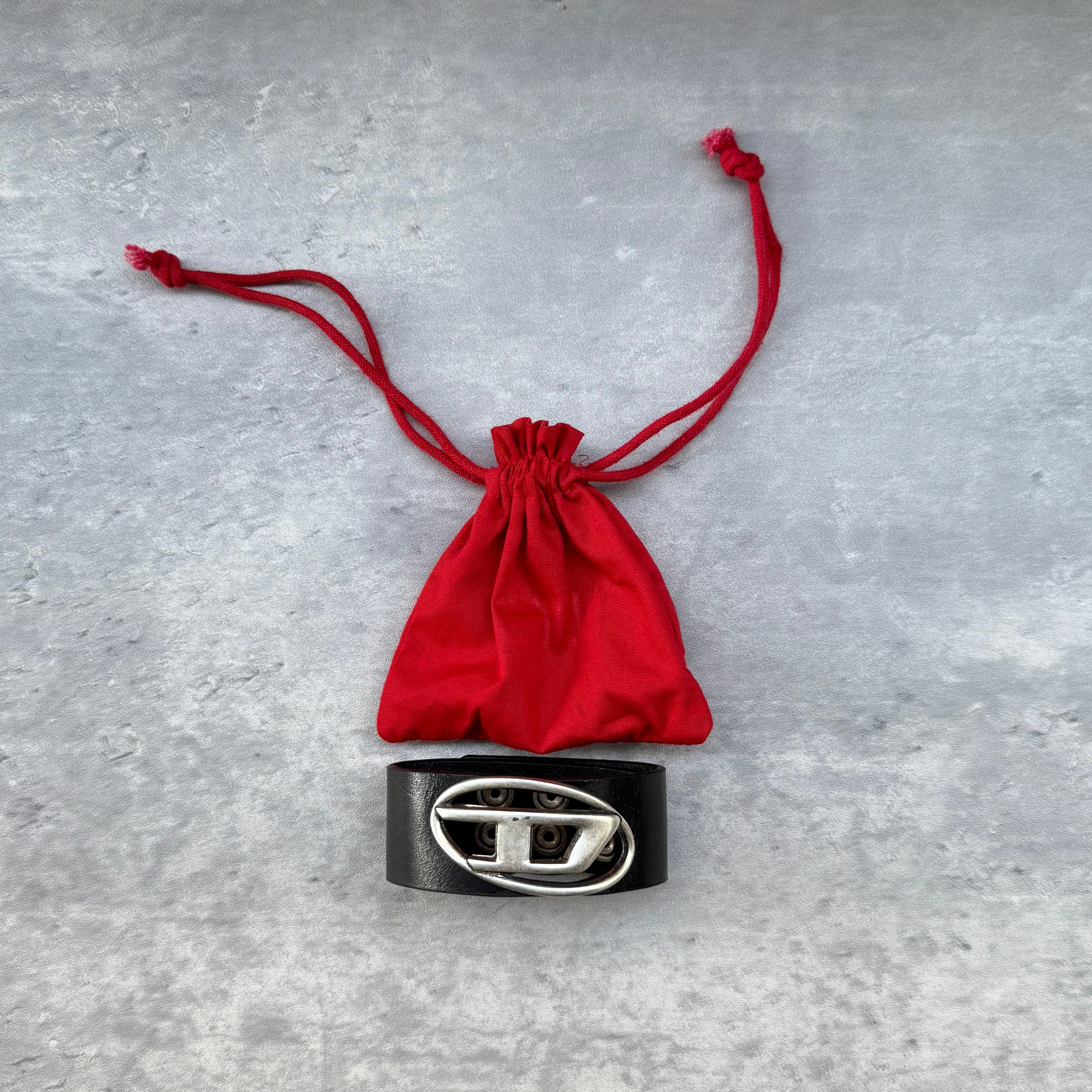 Pre-loved Diesel A-Balone bracelet in black resin with silver cut-out logo, slip-on cuff style, displayed with red drawstring pouch