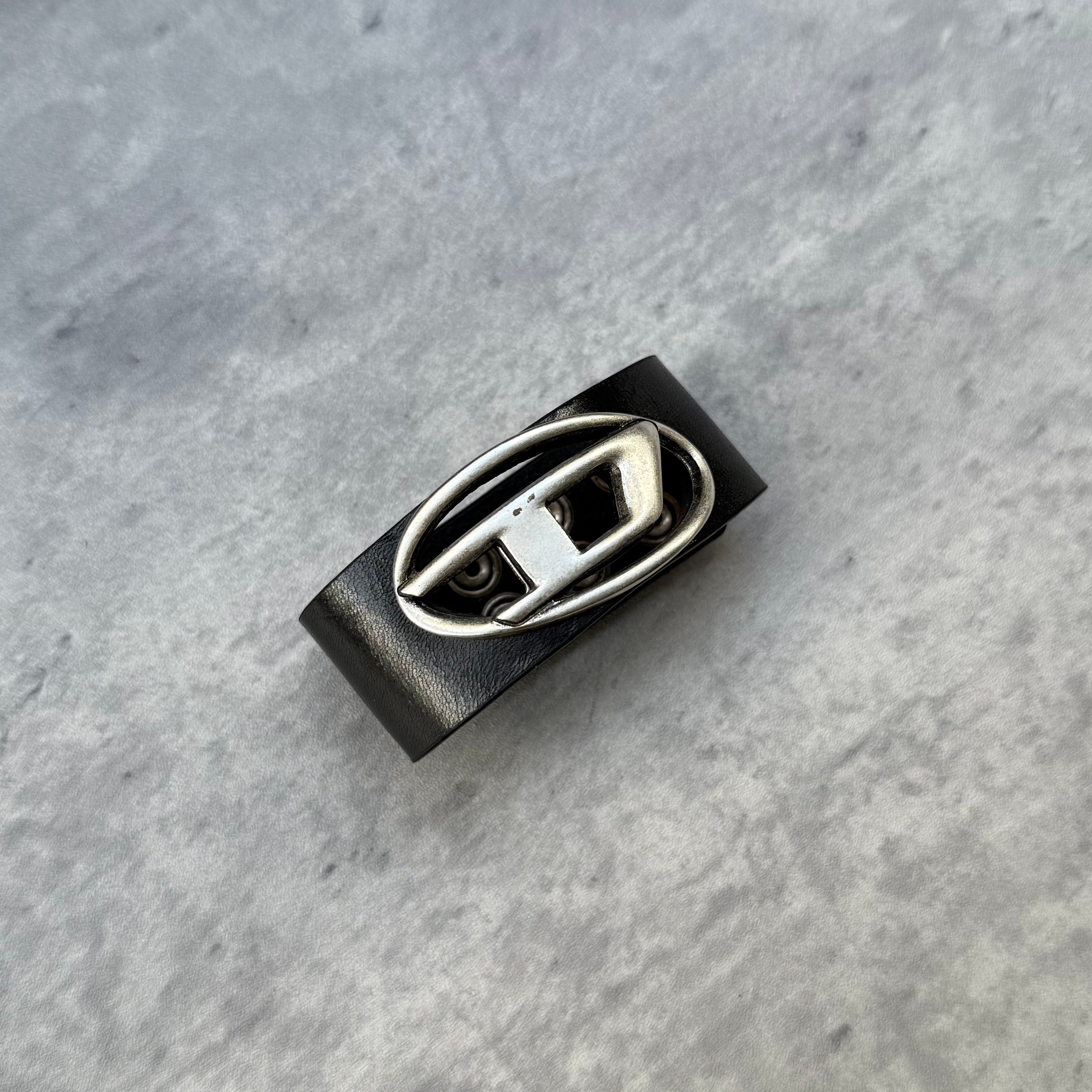 Pre-loved Diesel A-Balone bracelet in black resin with silver cut-out logo, slip-on cuff style, displayed with red drawstring pouch