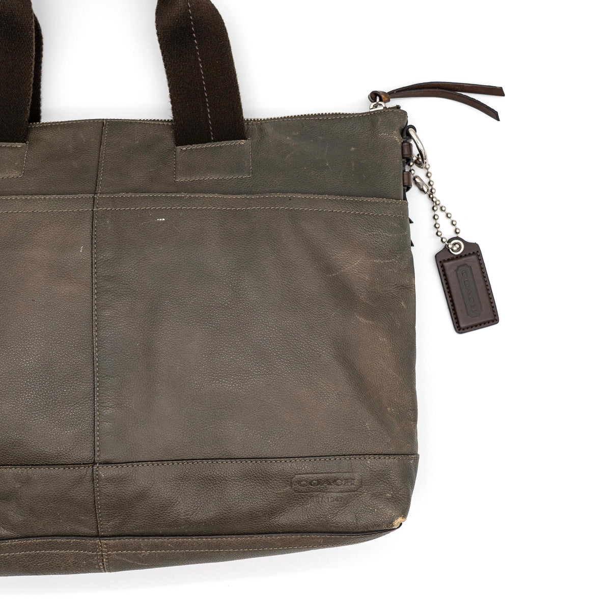 Coach brown leather tote bag with double handles and front zip pocket, shown on a white background.