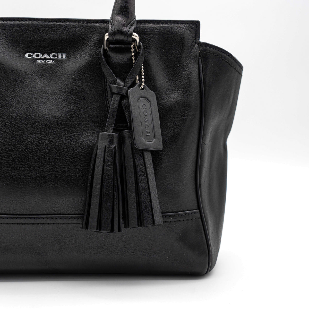 Coach Legacy Candace Carryall in black leather with double tassel charm and silver hardware, photographed against a white background.