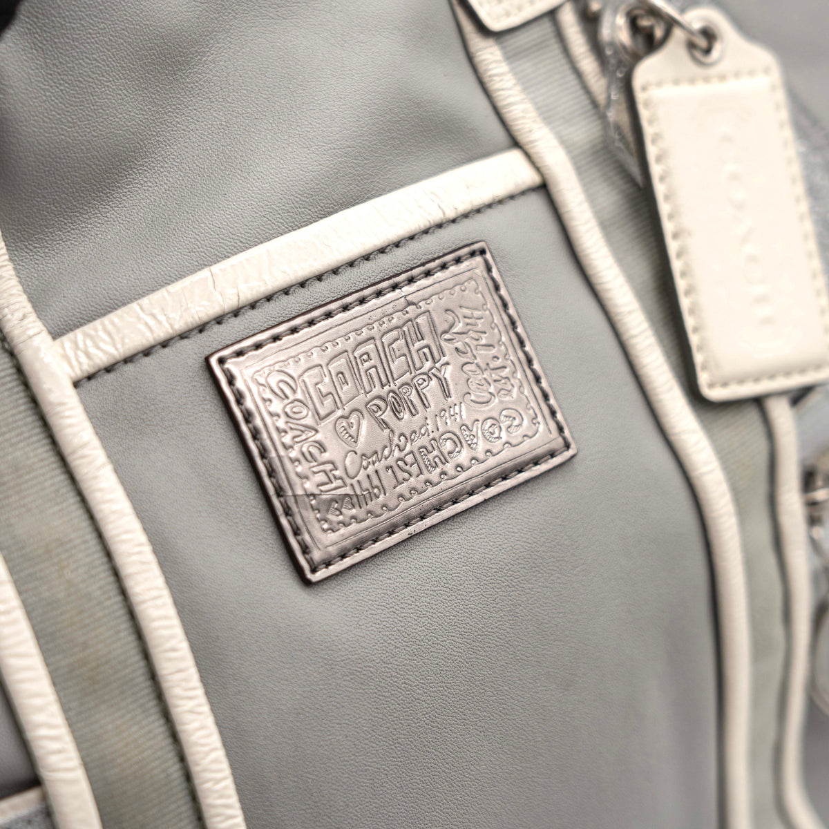 Coach Poppy Spotlight grey shoulder bag with double top handles, white trim, and detachable webbing strap, displayed on a white background.