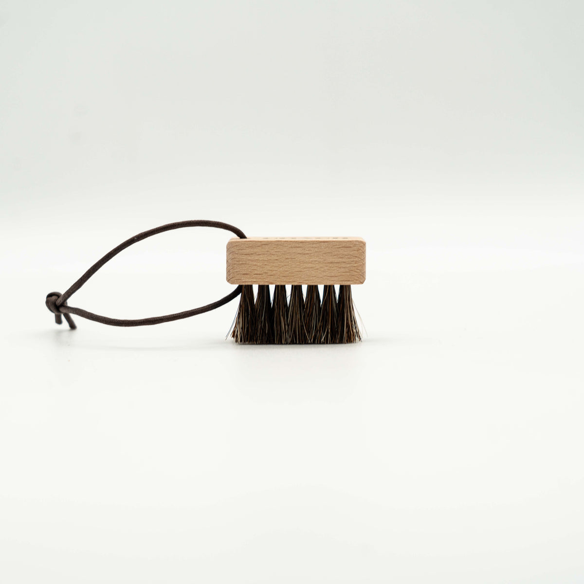 Coach horsehair leather care brush with wood handle and brown bristles, featuring a Coach logo and leather cord loop.