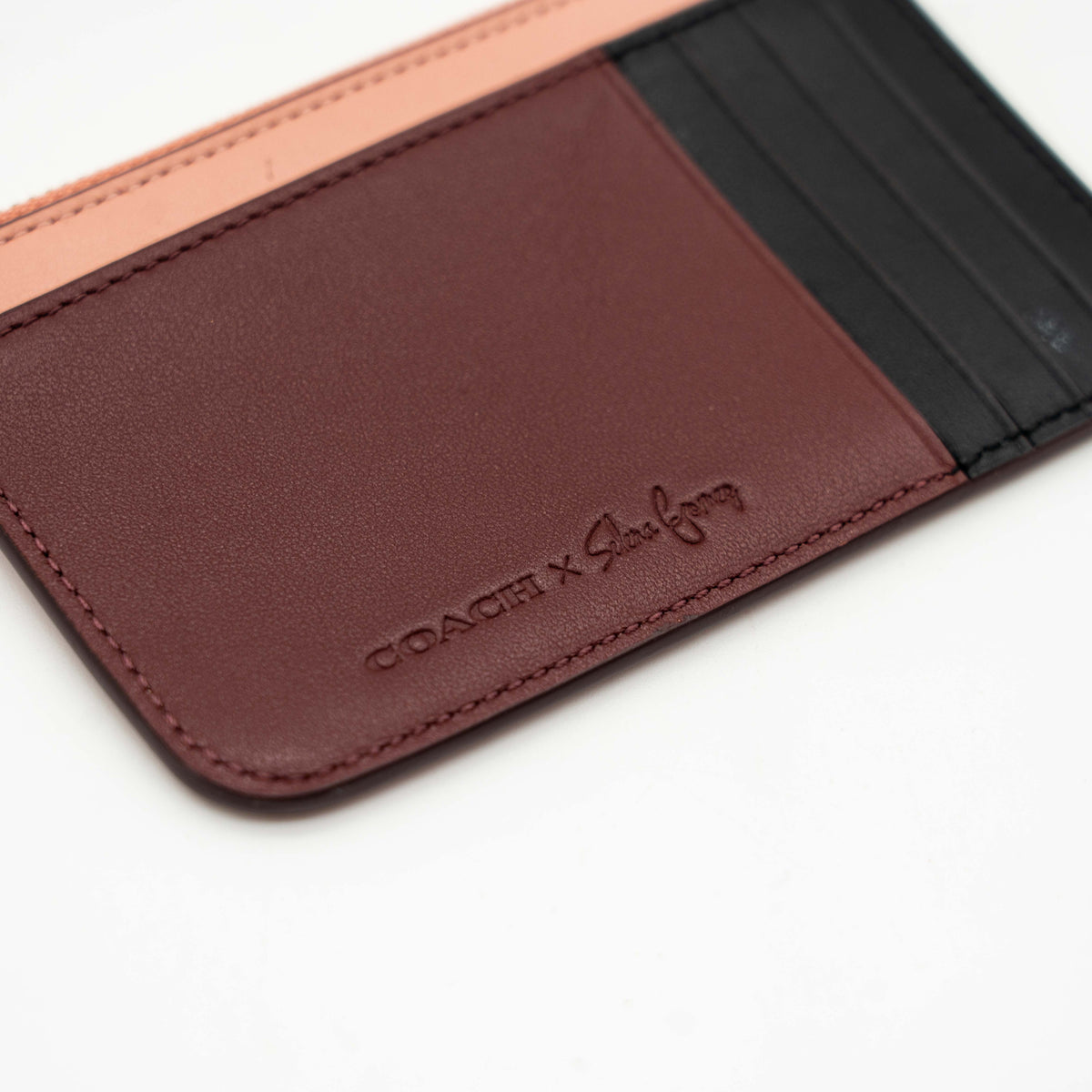 Coach x Selena Gomez colorblock zip card case in pink, burgundy, and black leather with gold hardware and script detail.