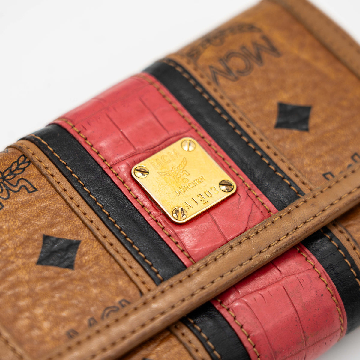 Front view of the MCM Cognac Visetos Monogram Stripe Trifold Wallet in brown with red and black accents and gold logo plaque.