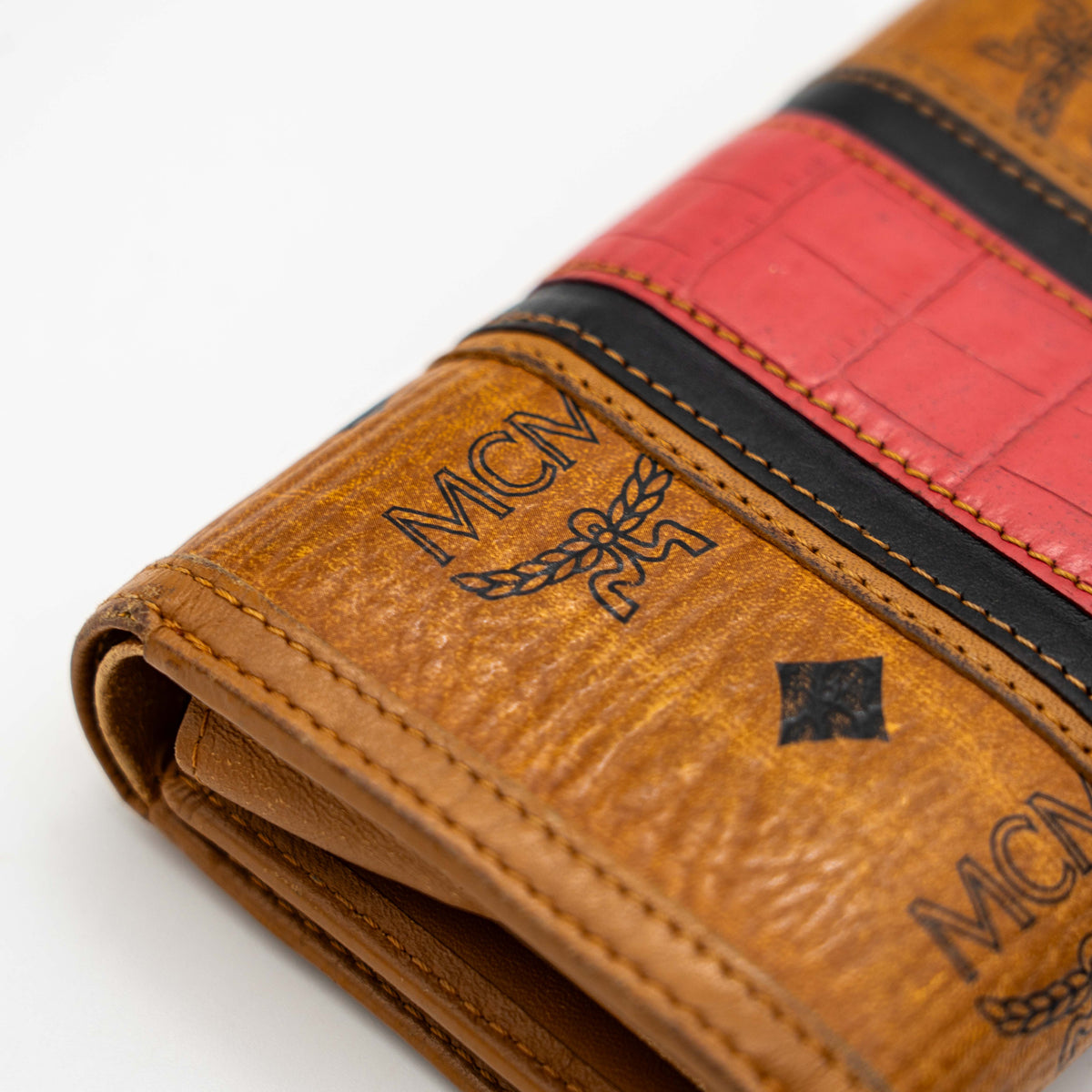 Front view of the MCM Cognac Visetos Monogram Stripe Trifold Wallet in brown with red and black accents and gold logo plaque.