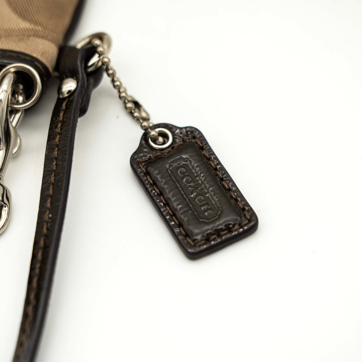 Coach brown monogram wristlet with silver badge and detachable leather strap, photographed on a white background.