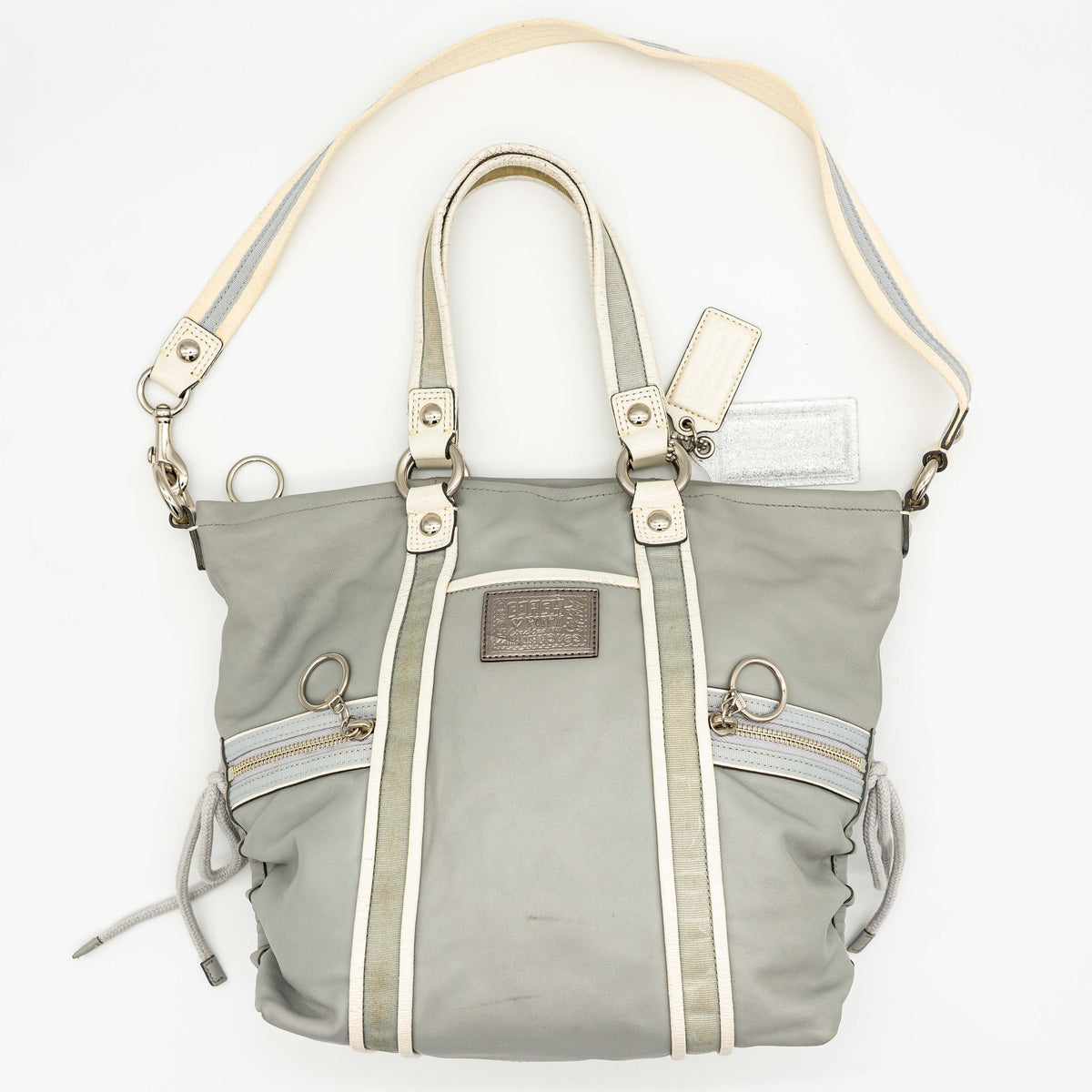 Coach Poppy Spotlight grey shoulder bag with double top handles, white trim, and detachable webbing strap, displayed on a white background.