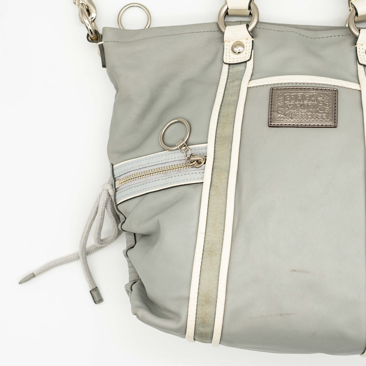 Coach Poppy Spotlight grey shoulder bag with double top handles, white trim, and detachable webbing strap, displayed on a white background.