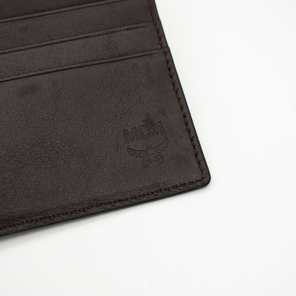 MCM dark brown leather bifold wallet with embossed Visetos monogram pattern shown against a white background.