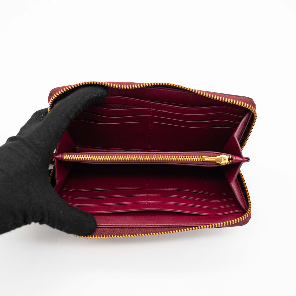 Coach Signature Accordion Zip Wallet in burgundy monogram canvas with leather trim and gold zip, photographed against a clean white background.