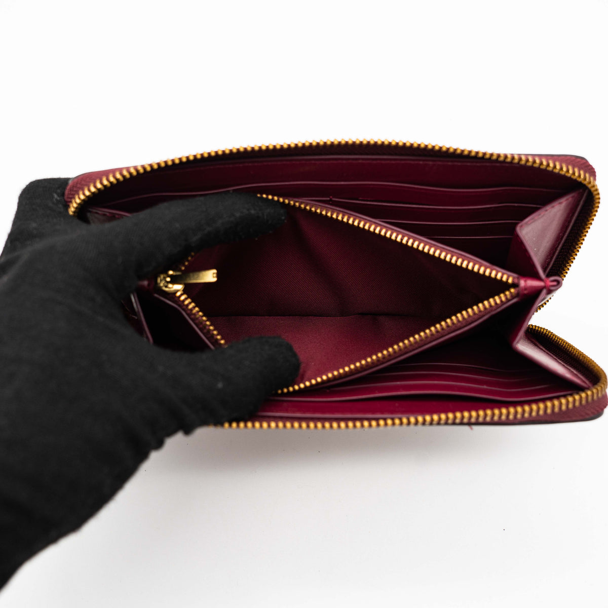 Coach Signature Accordion Zip Wallet in burgundy monogram canvas with leather trim and gold zip, photographed against a clean white background.