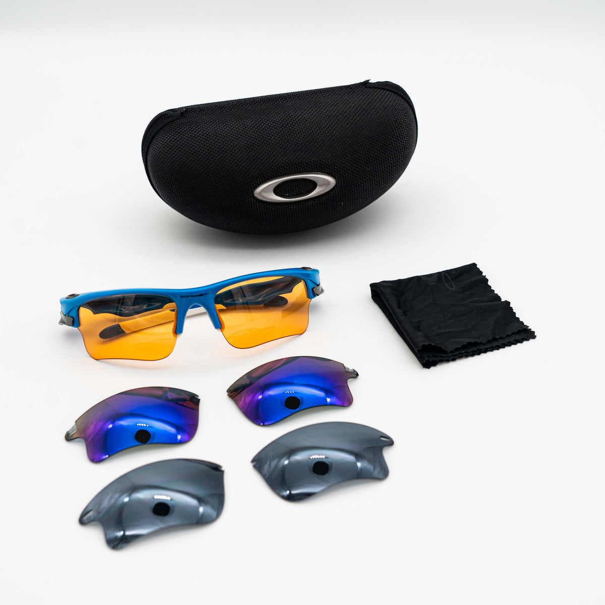 Oakley Fast Jacket OO9156-04 sunglasses in blue with orange lenses, displayed with two extra pairs of lenses, cleaning cloth and a black Oakley hard case.