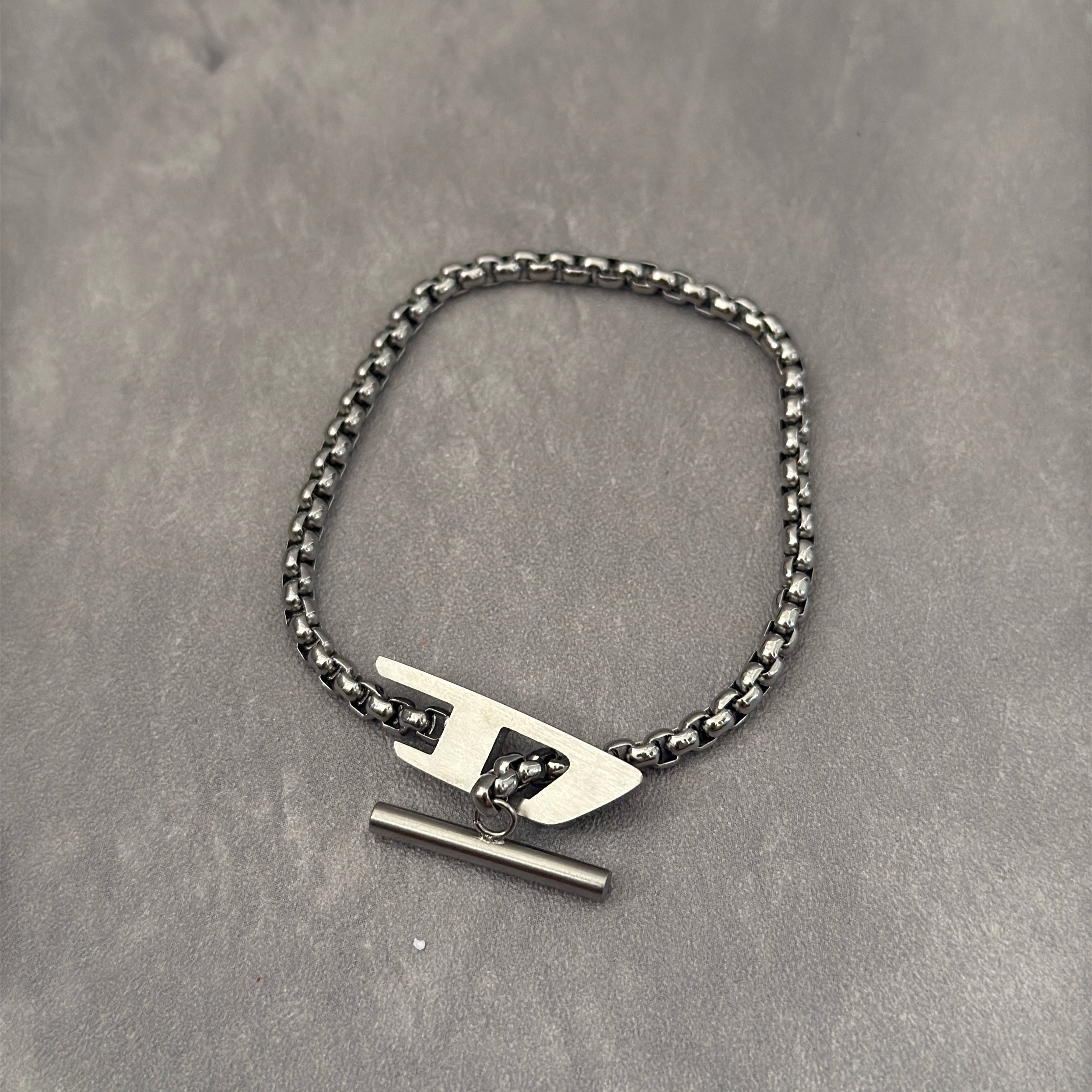 Diesel Signature D-Logo Stainless Steel Bracelet, featuring a silver-tone chain-link design with a bold Diesel "D" logo and a T-bar closure.