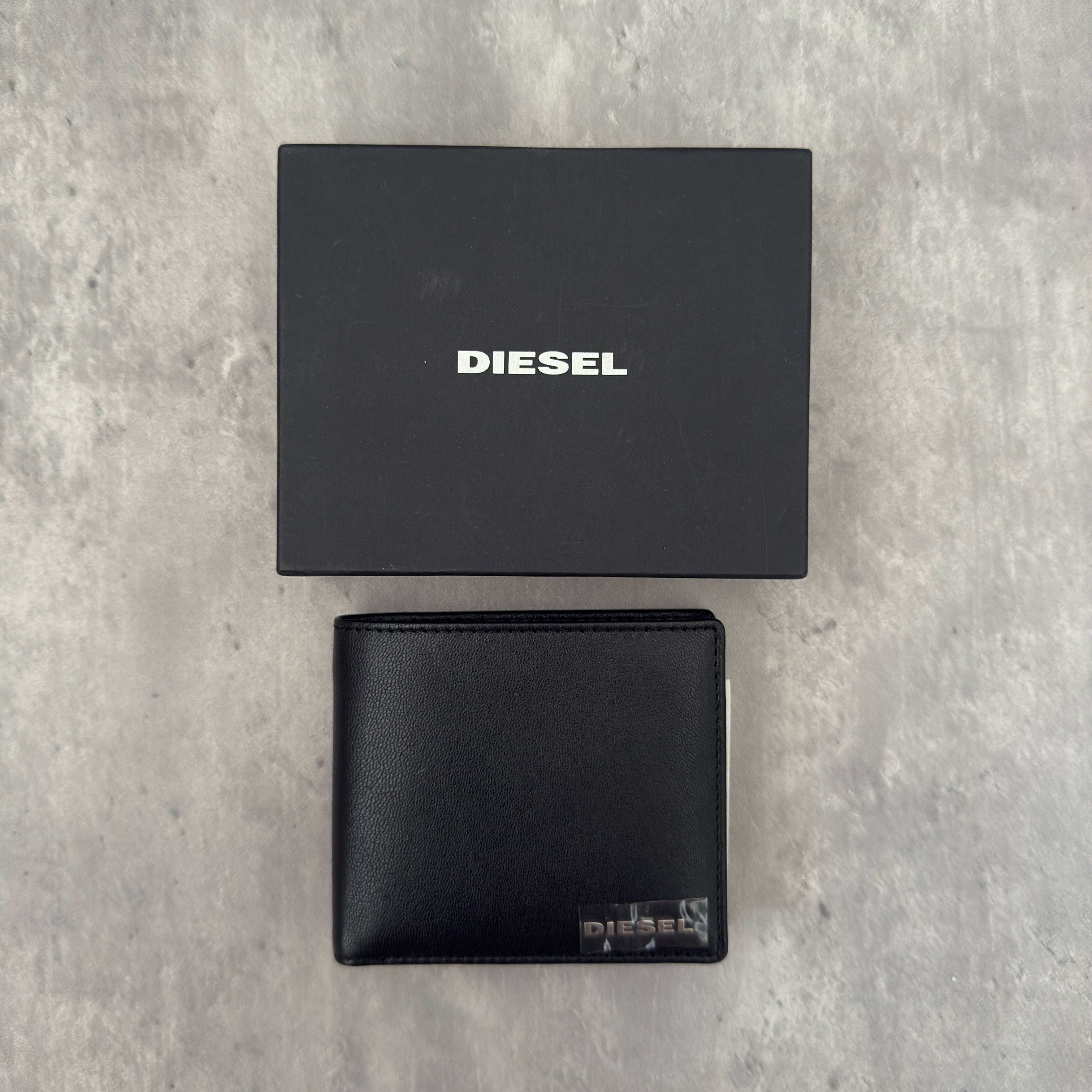 Diesel Signature Leather Wallet in black with contrast orange interior, featuring a metal logo plaque and multiple compartments.