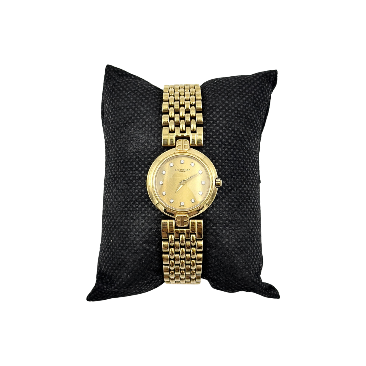 Balenciaga BB Quartz gold watch with a round dial, diamond-shaped hour markers, and a gold link bracelet displayed on a black cushion.