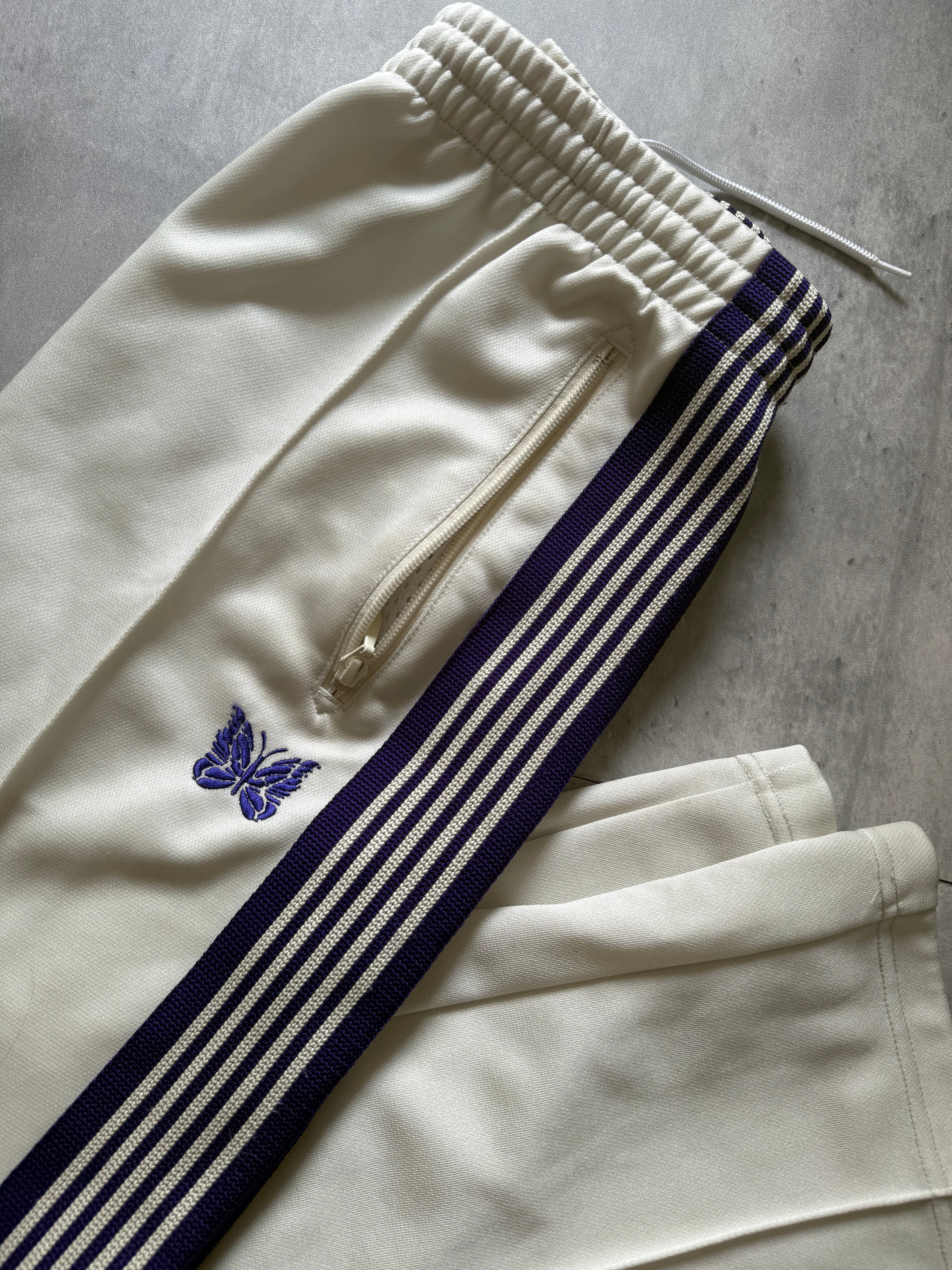 Needles Track Pants White and Purple, featuring striped taping and embroidered butterfly logo with zippered pockets.