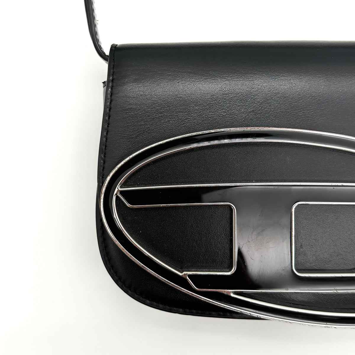 Diesel 1DR Shoulder Bag in black leather with a bold silver and black D logo plaque on the front flap.