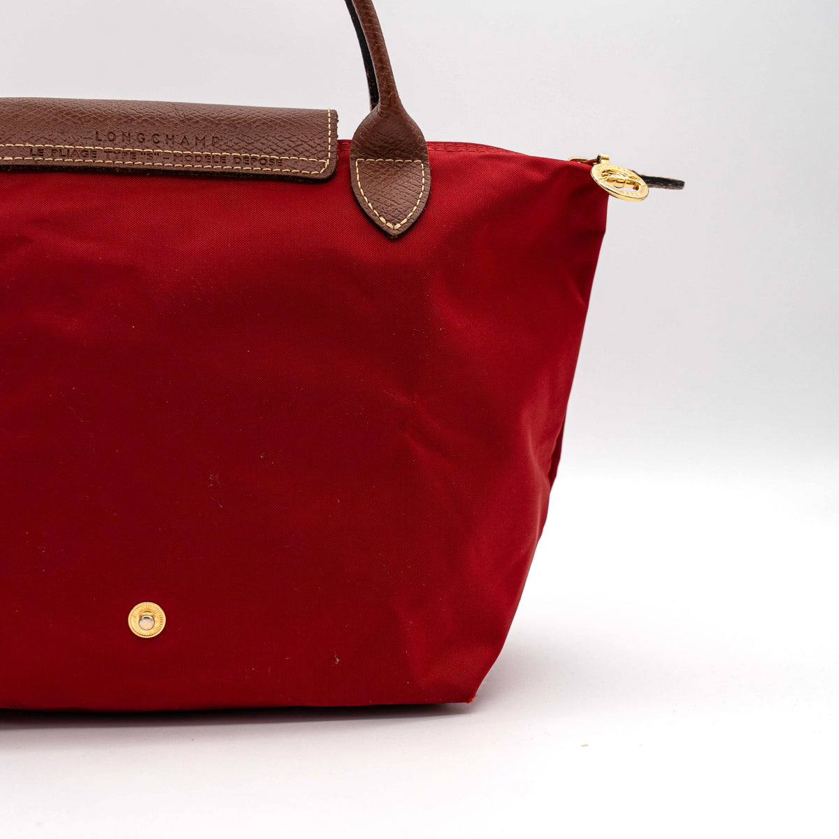 Longchamp Le Pliage handbag in red nylon with brown leather handles and gold-tone accents, photographed on a white background.
