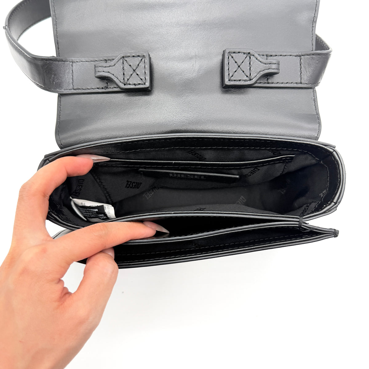 Diesel 1DR Shoulder Bag in black leather with a bold silver and black D logo plaque on the front flap.