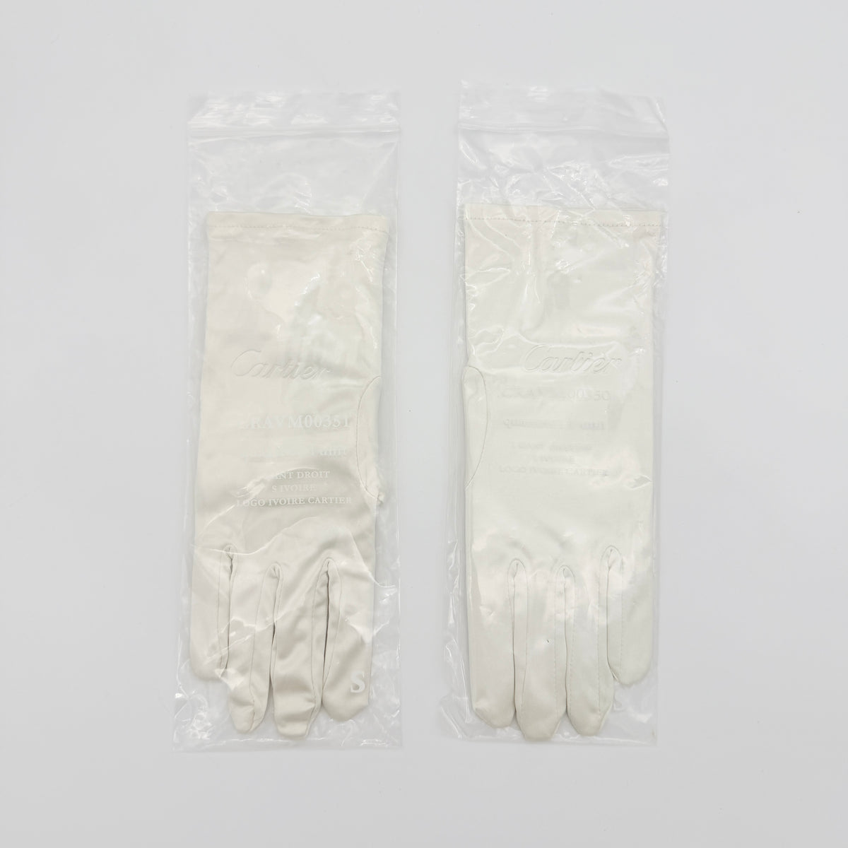 Pair of Cartier ivory gloves with signature script logo embroidery displayed on a flat white background.