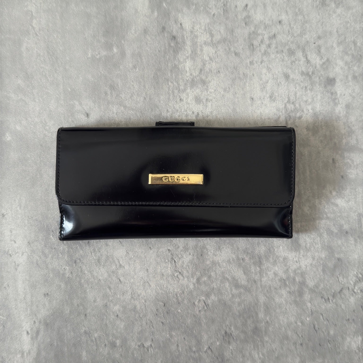 Gucci Continental Wallet in black patent leather, featuring a gold-tone Gucci logo, multiple card slots, and a spacious interior, epitomizes luxury and functionality.