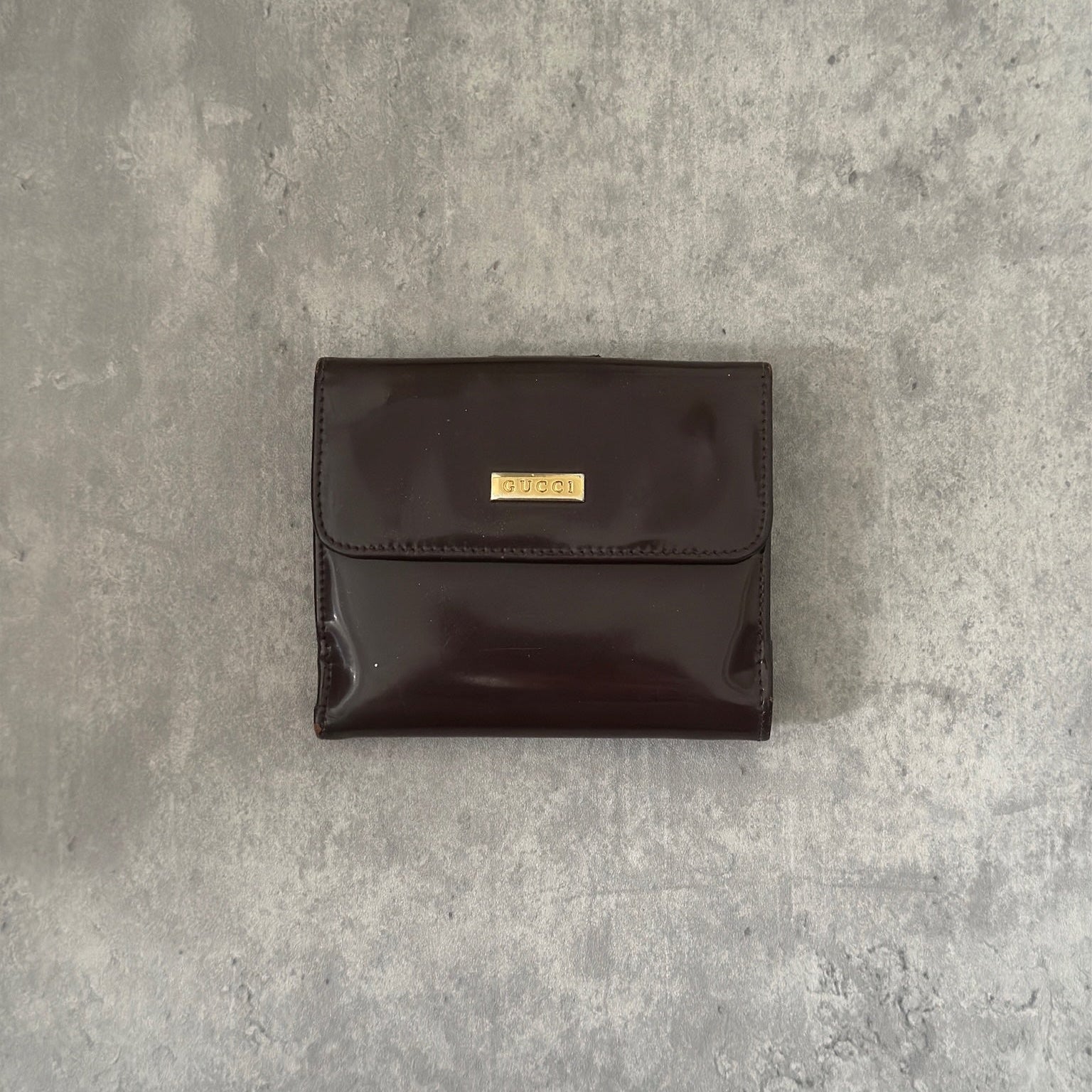 Gucci brown patent leather bifold wallet with multiple card slots and bill compartments, showcasing classic style and luxury.