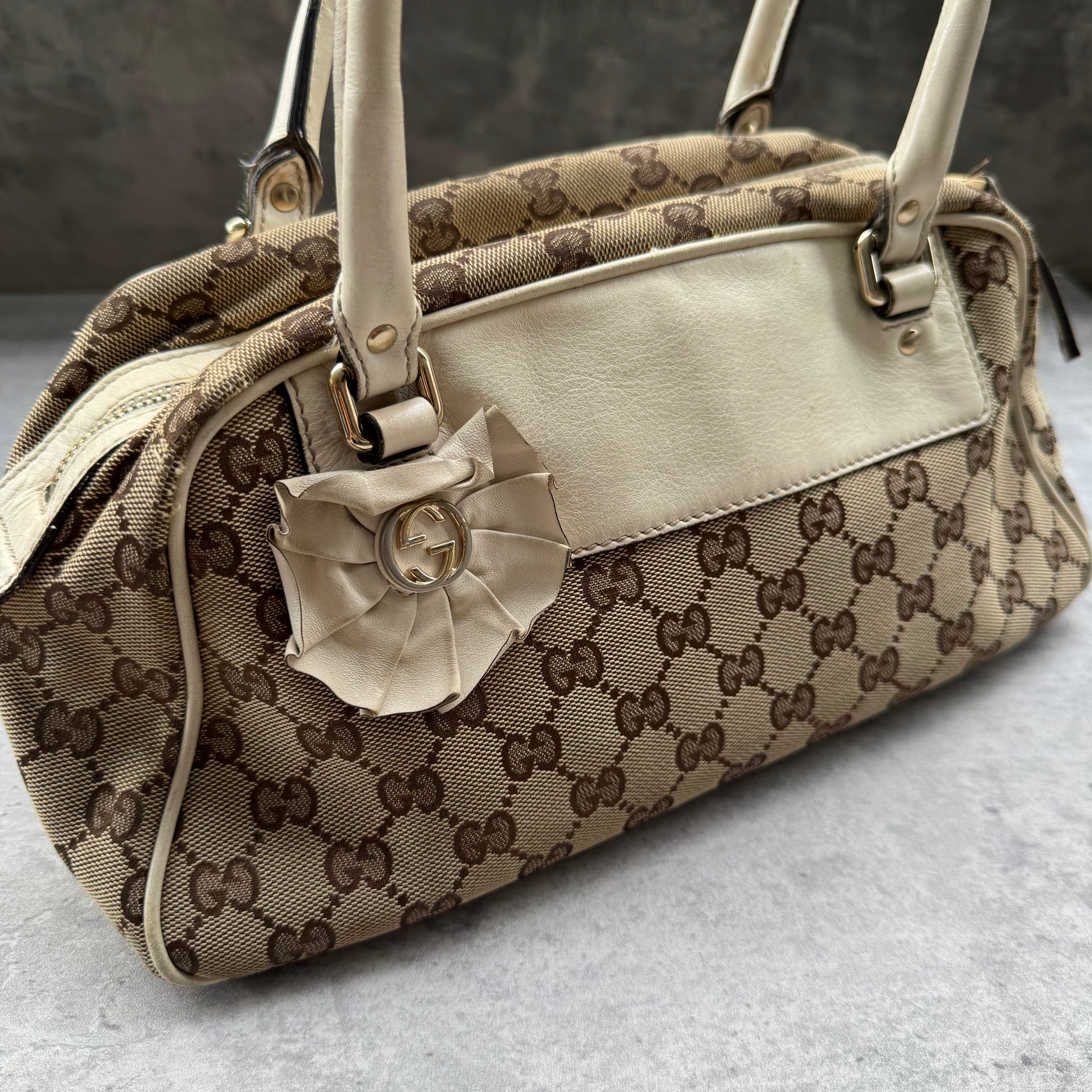 Gucci GG Canvas Trophy Boston Bag in beige monogram canvas with cream leather trim and floral GG emblem detail.