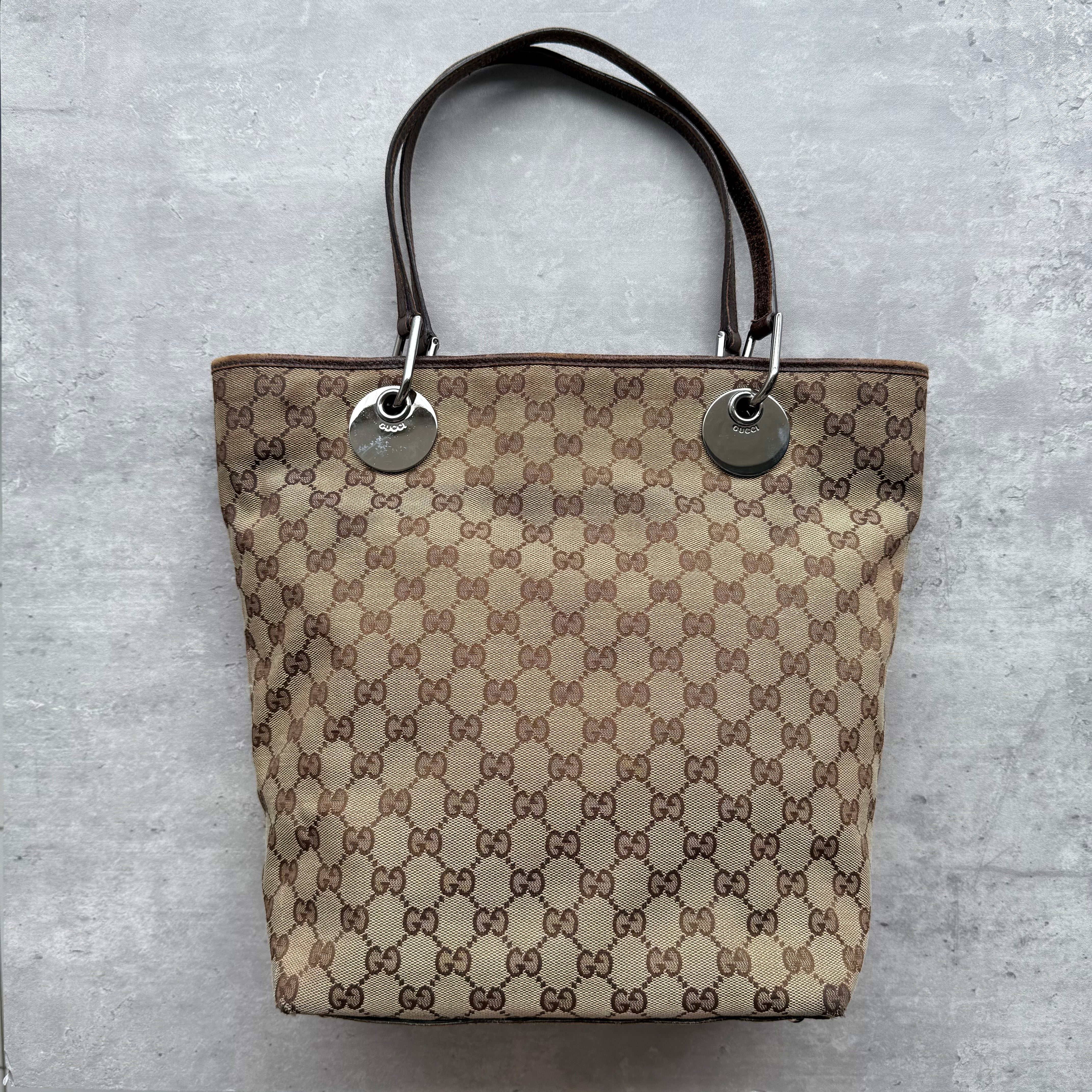Gucci GG Monogram Tote Bag in beige canvas with silver eyelet hardware, brown leather straps, and open top with interior pockets