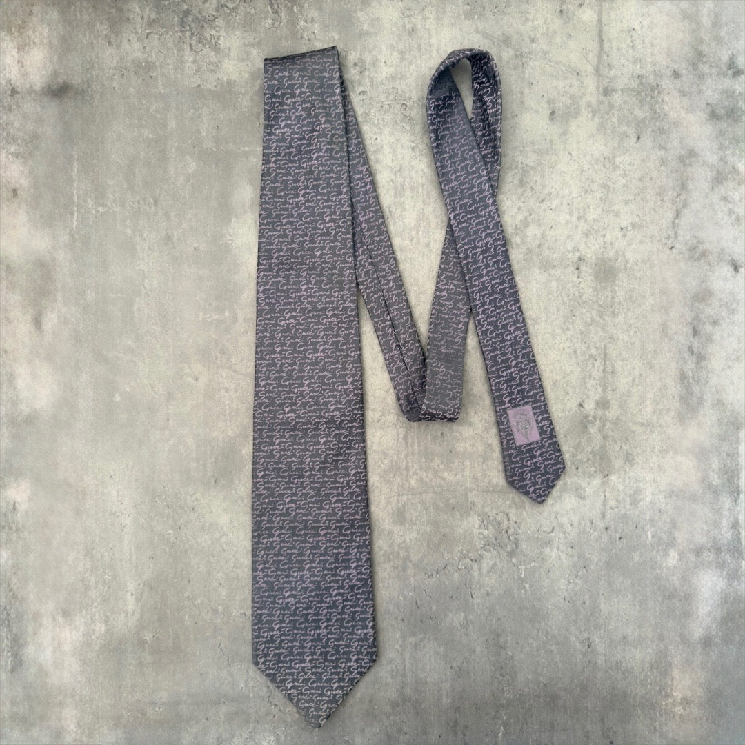 Vintage Gucci silk tie in gray with purple interlocking 'G' pattern and Gucci crest, exemplifying classic elegance and luxury style.