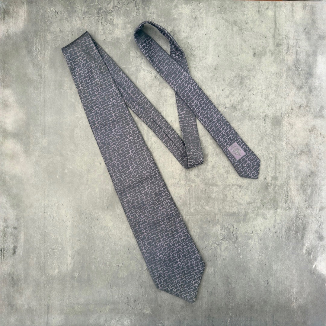 Vintage Gucci silk tie in gray with purple interlocking 'G' pattern and Gucci crest, exemplifying classic elegance and luxury style.