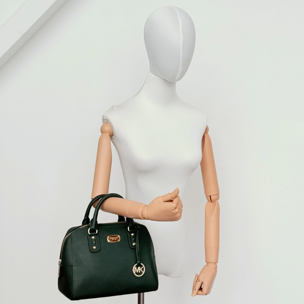 Michael Kors dark green Saffiano leather dome satchel with gold hardware and detachable strap, shown against a white background.