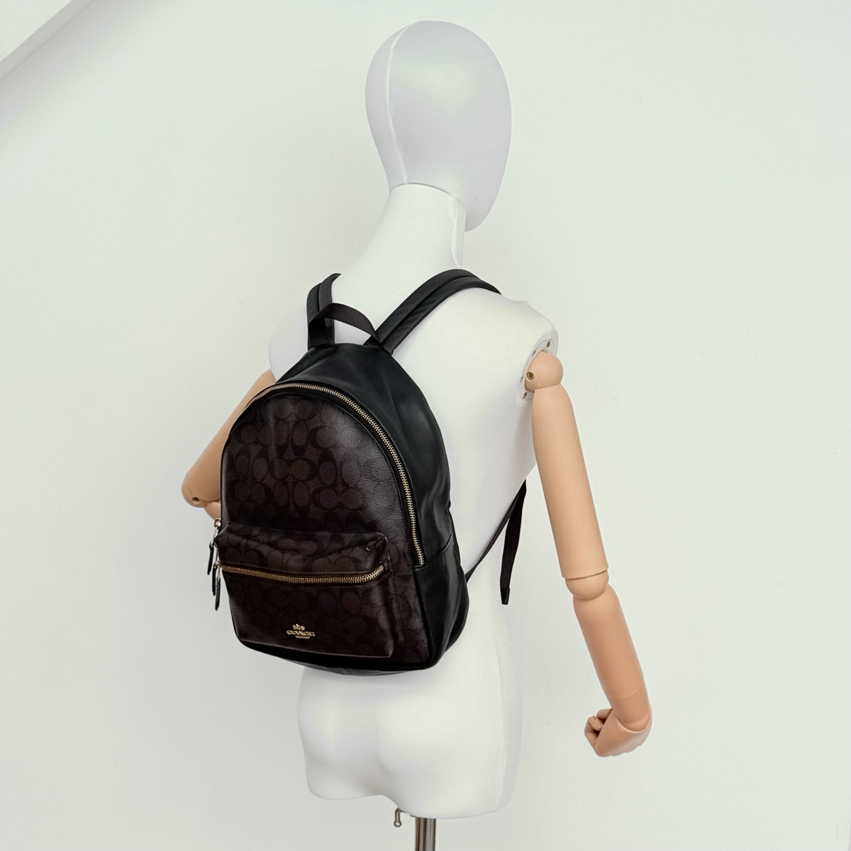 Coach Signature Charlie Backpack in brown and black canvas with gold-tone hardware and front zip pocket.