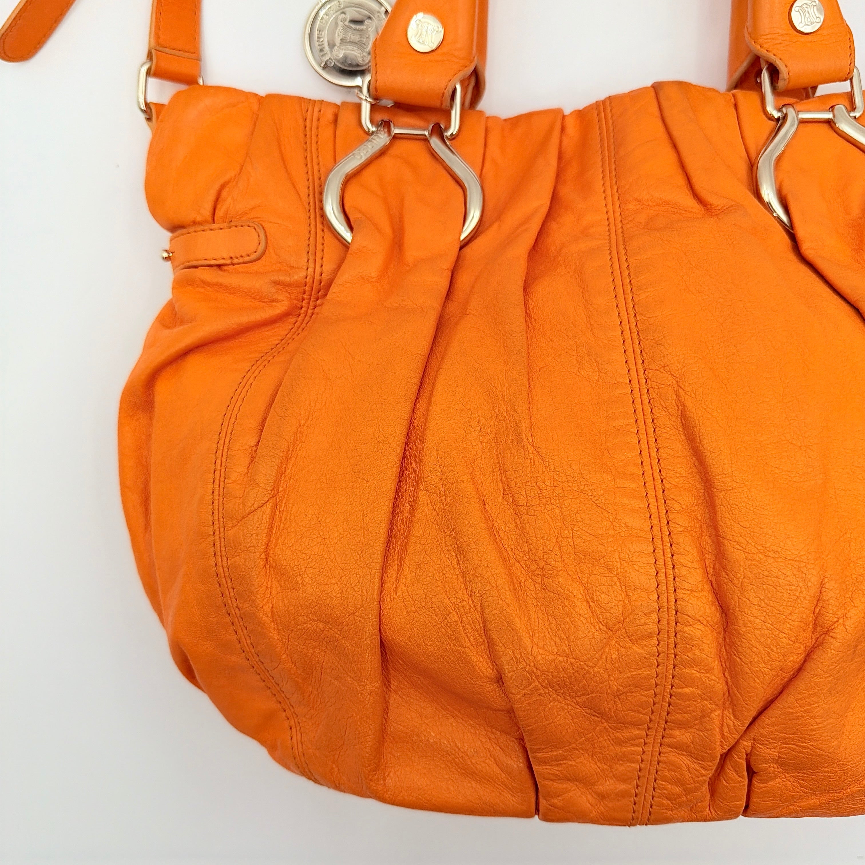 Celine 2Way Shoulder Bag in vibrant orange leather with silver-tone hardware and pleated detailing, shown with both top handles and an adjustable strap.